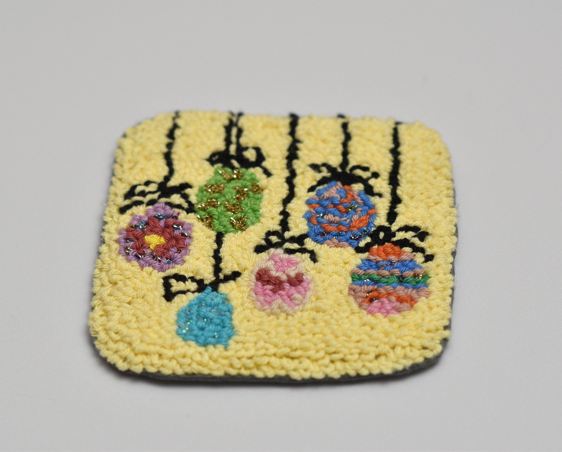 Square woven Easter Egg coaster with floral design on a gray background