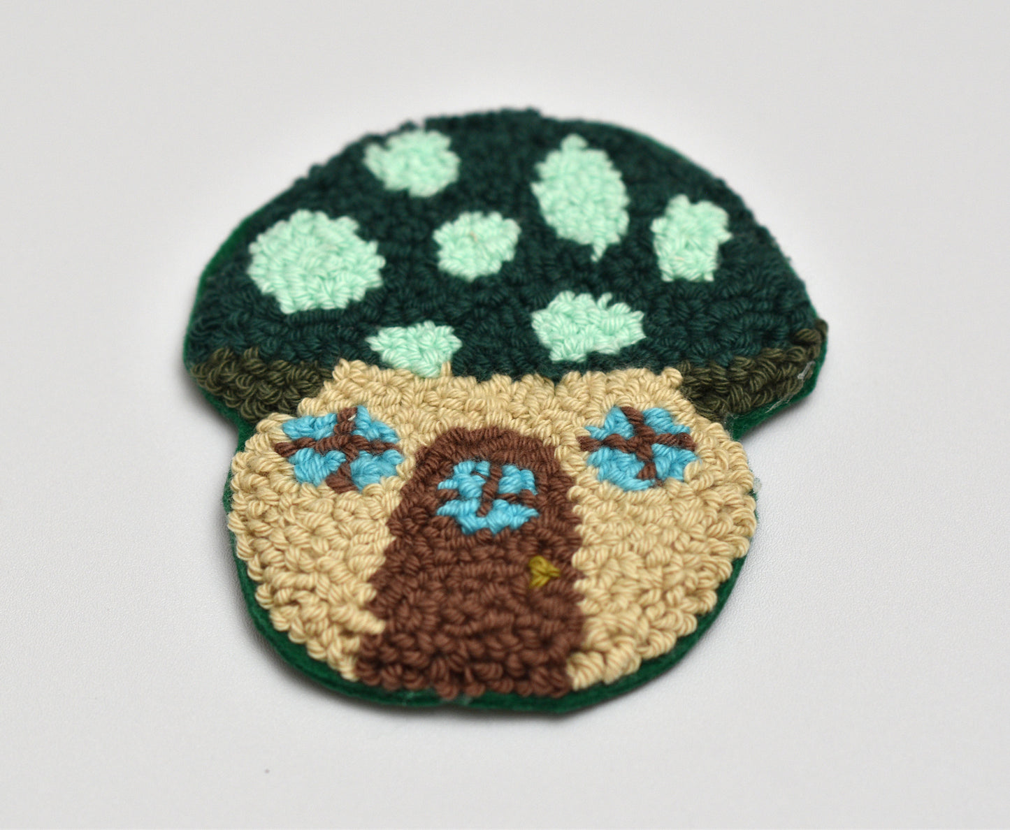 Mushroom-shaped punch needle coasters on a light gray background