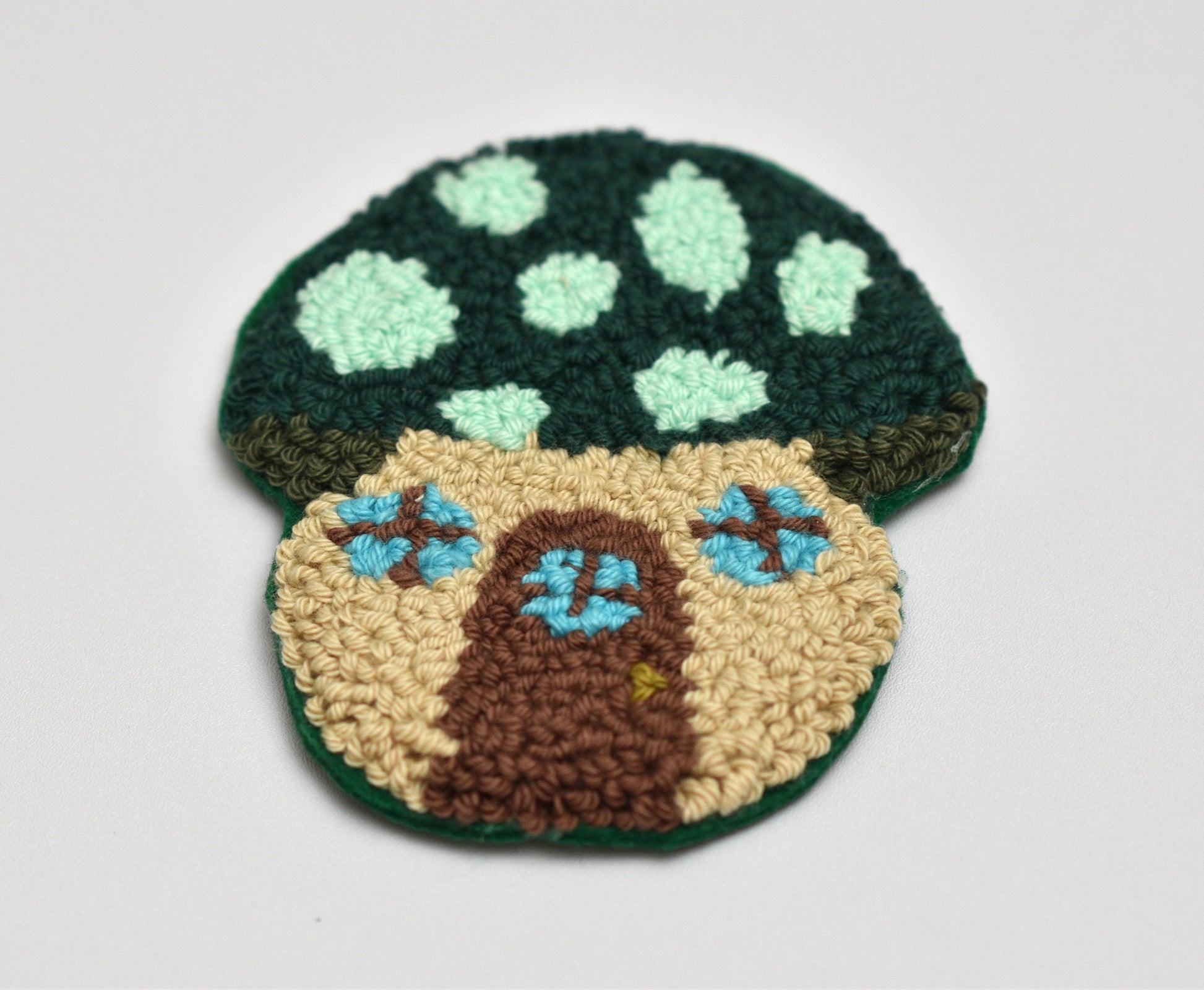 Mushroom-shaped punch needle coasters on a light gray background