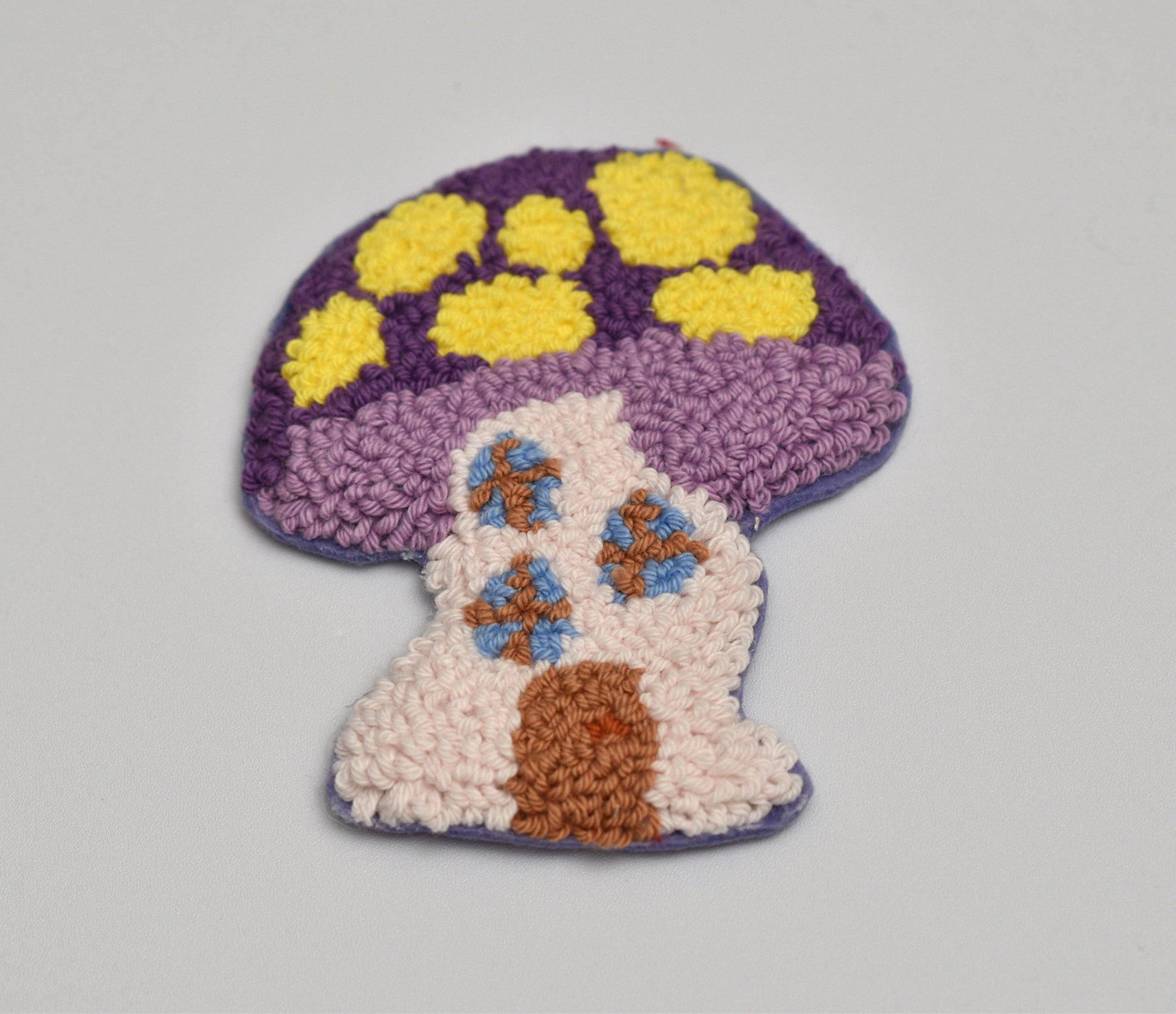 Decorative punch needle mug rug with mushroom design on a gray background