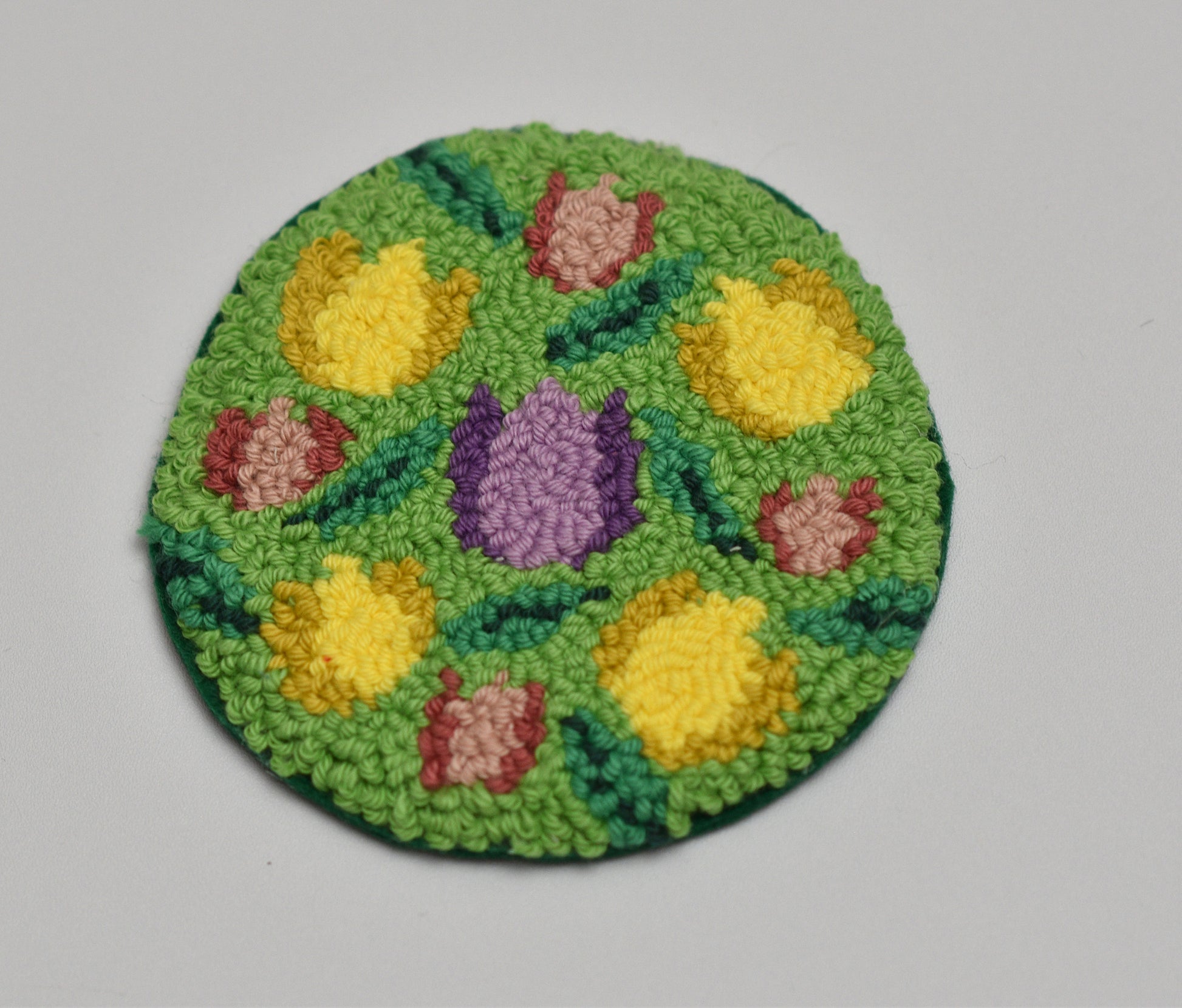Circular woven mug rug with floral tulip patterns on a gray background