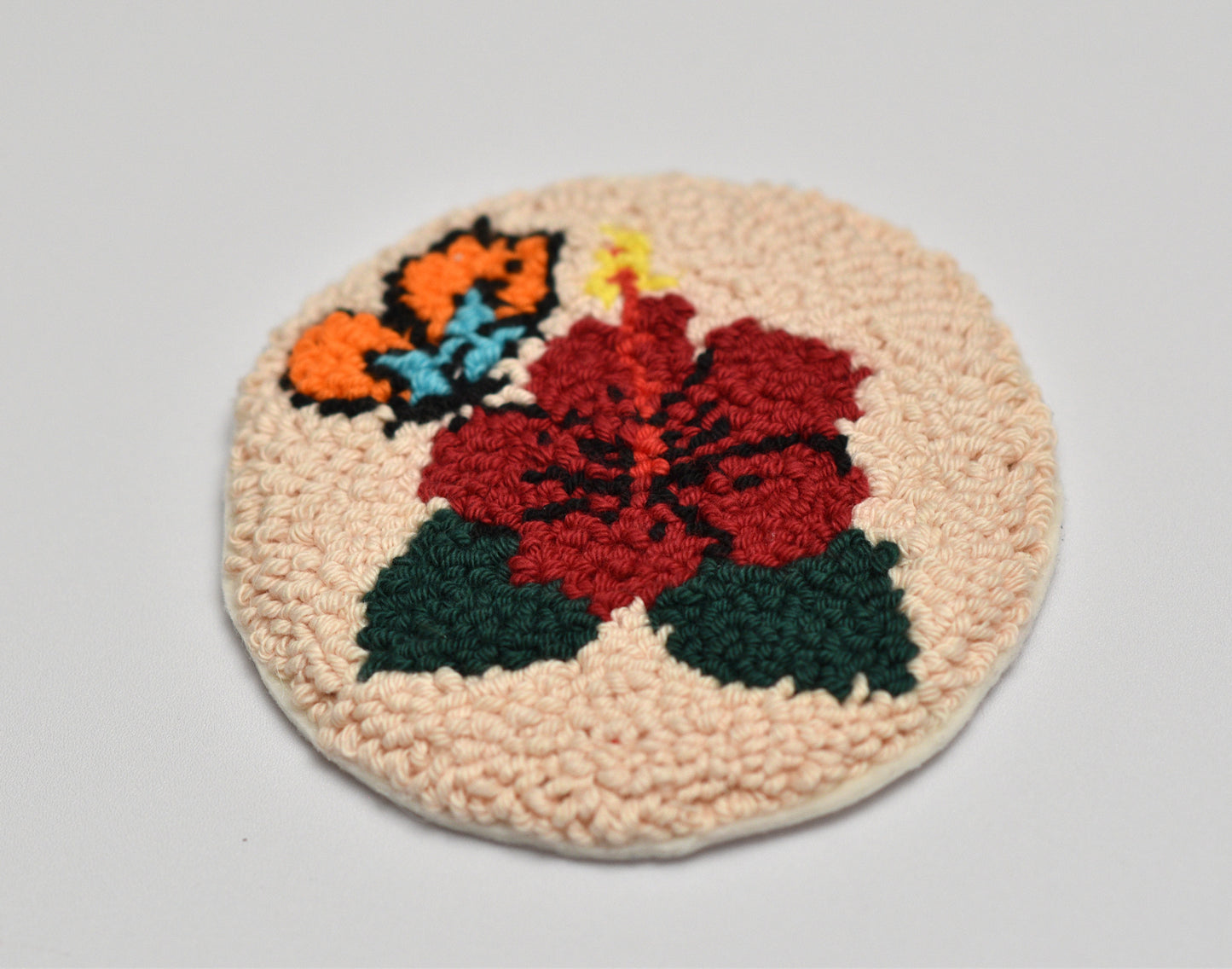 Round woven coaster with floral hibiscus design on a light gray background