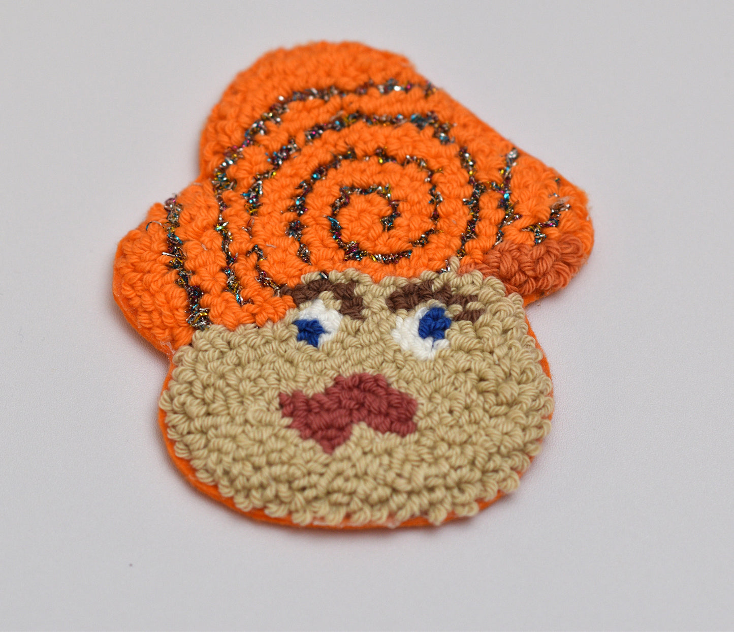 Punch needled coaster with mushroom character with orange hair and beige face on a light gray background