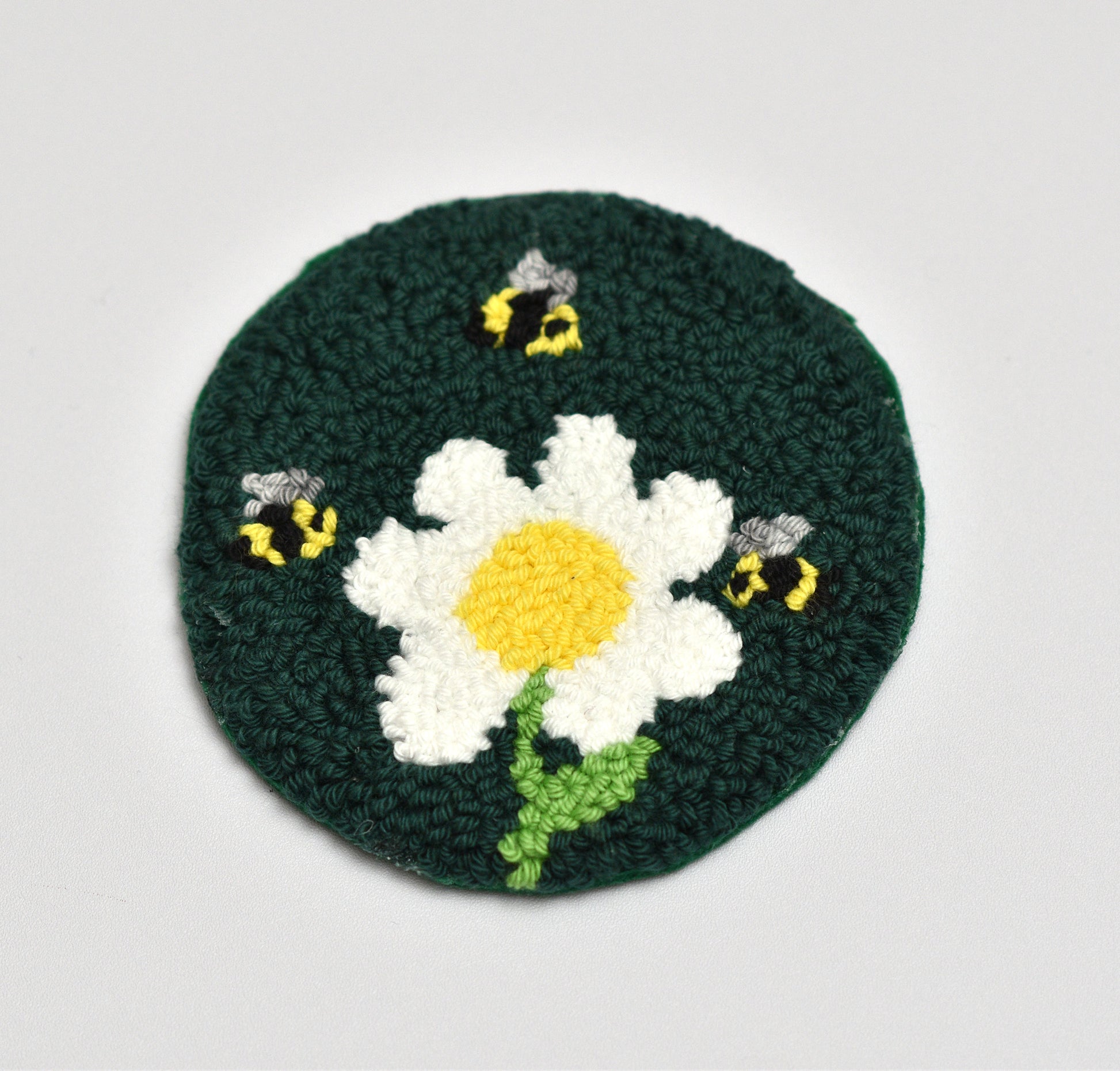 Embroidered coaster with a daisy and bees design on a white background
