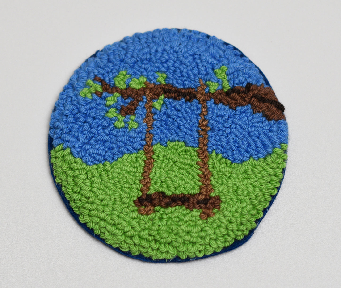 Round mug rug with a tree and swing design on a plain background
