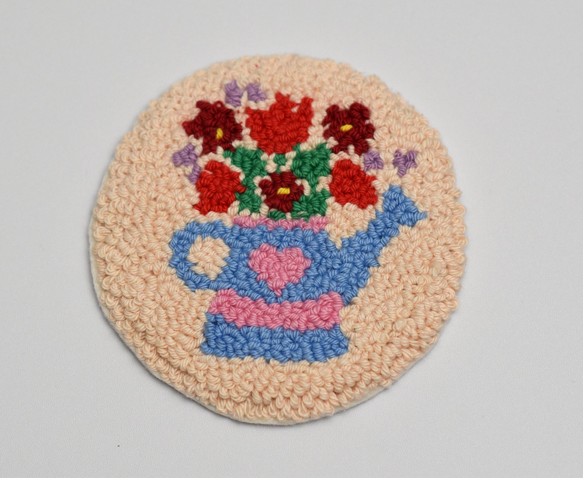 Crocheted rug with a watering pot and flowers design on a plain background