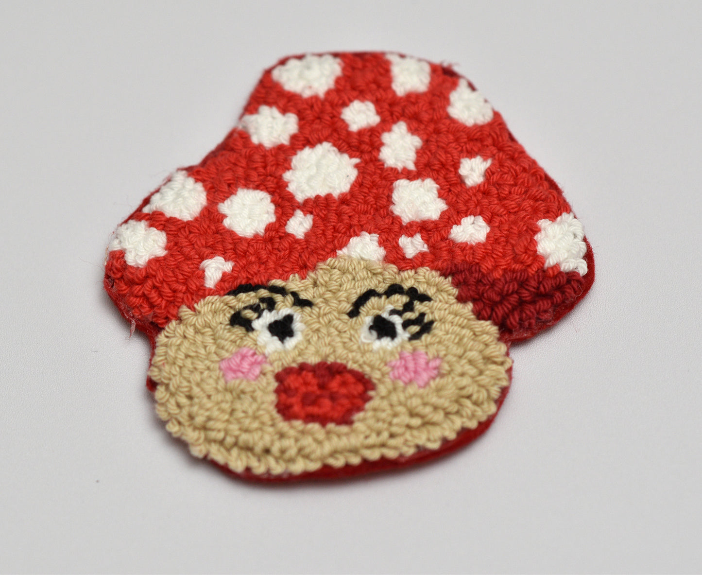 Embroidered coaster with mushroom design with a face on a white background