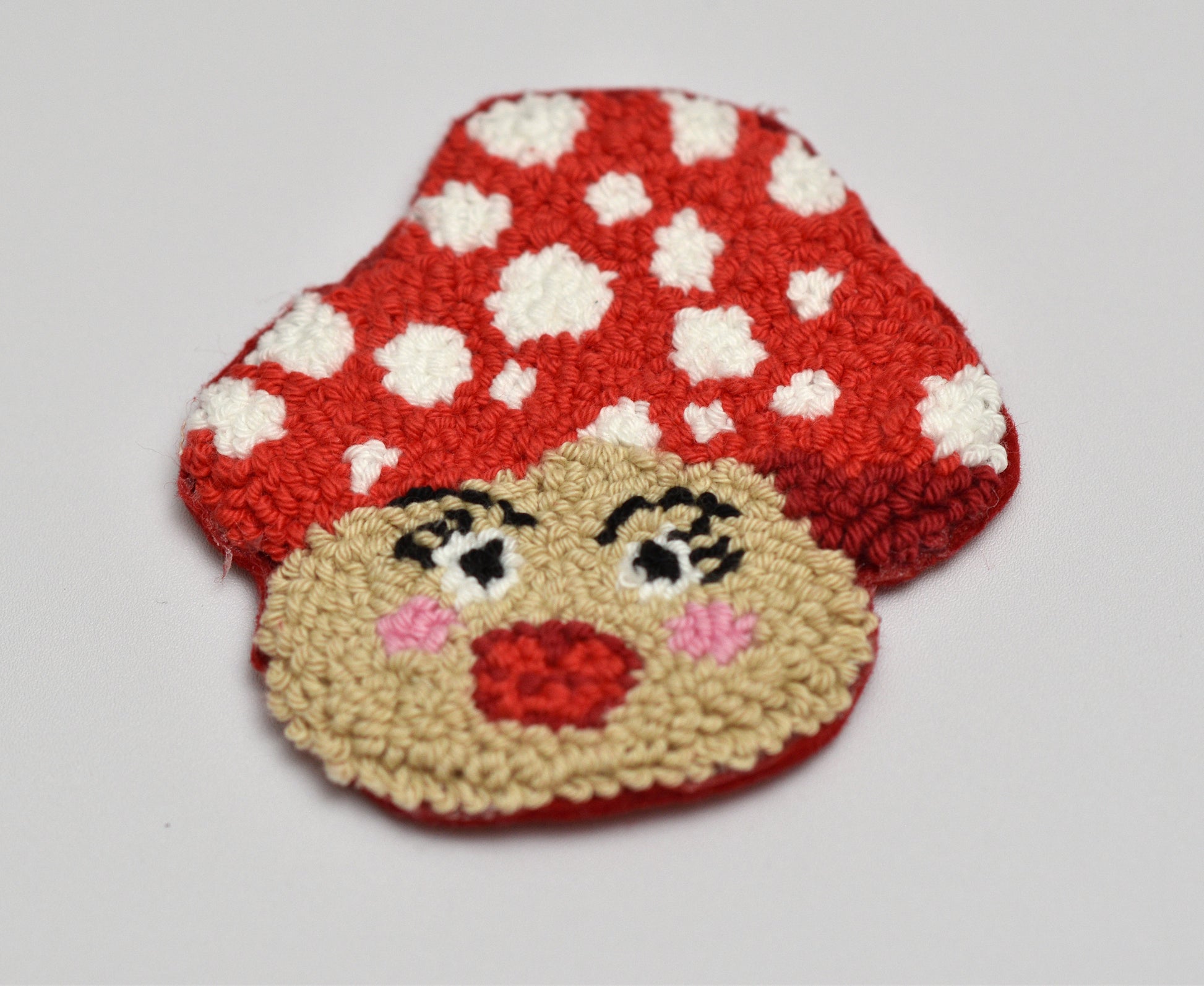 Embroidered coaster with mushroom design with a face on a white background