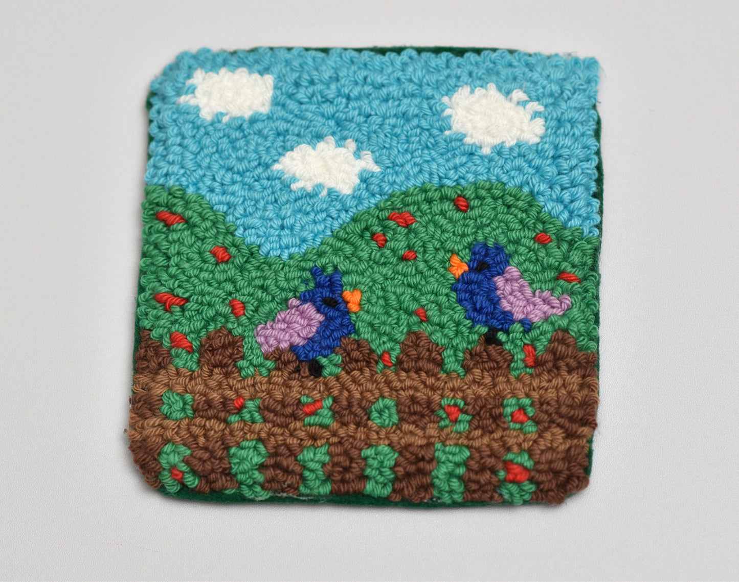 Handmade mug rug with a landscape design featuring two birds, green hills, and blue sky.