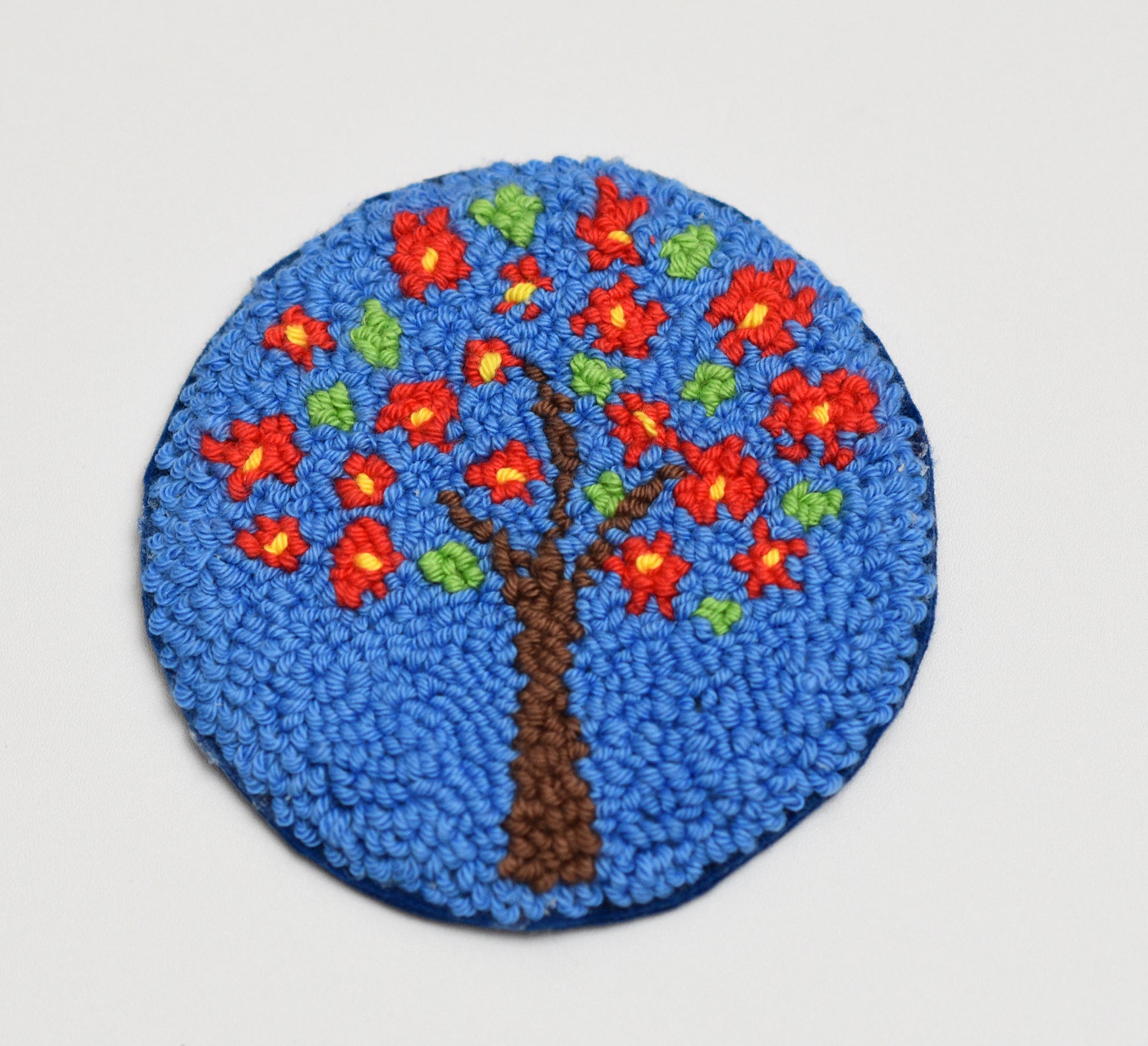 Round mug rug with a tree design featuring red flowers and green leaves on a blue background.
