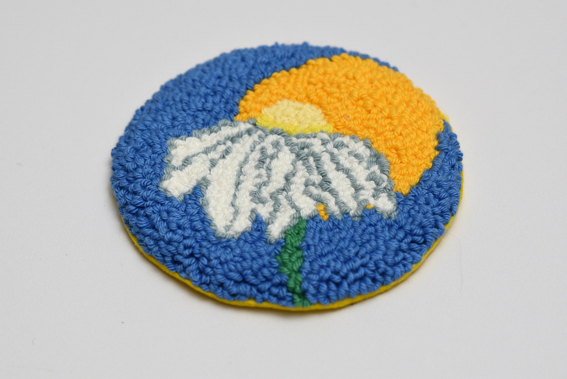 Round embroidered coaster with a flower daisy design on a blue background