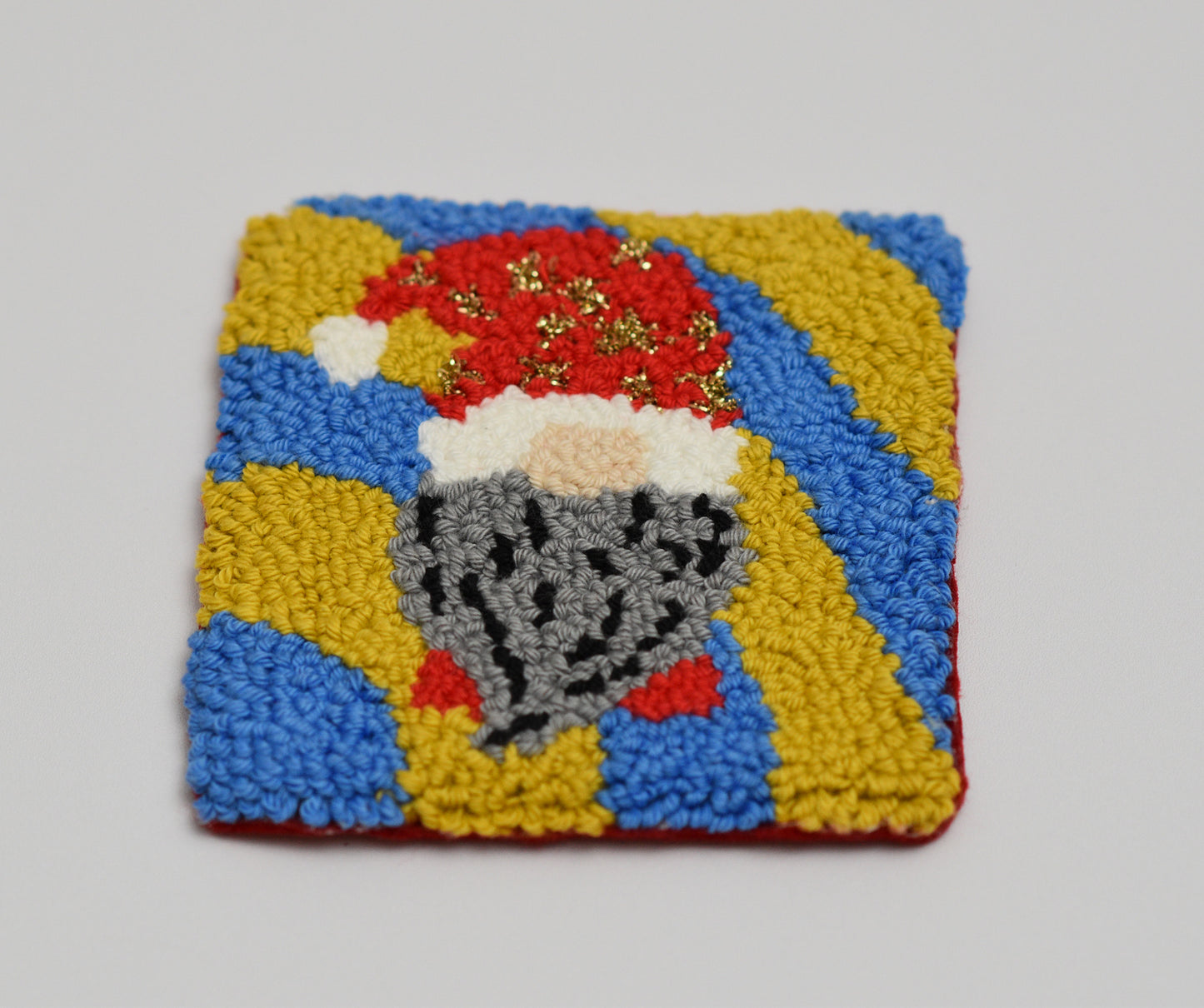 Square punch needle coaster with a gnome wearing a Santa hat on a gray background