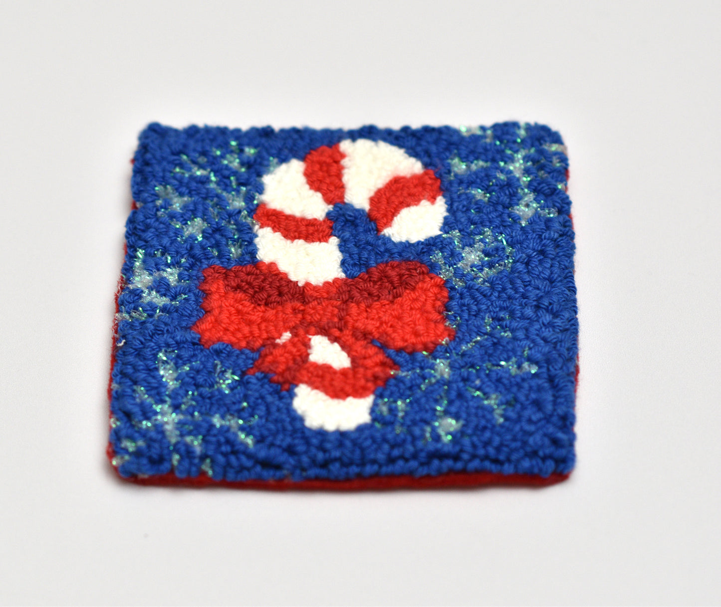 Punch needled coaster with candy cane design on a blue background