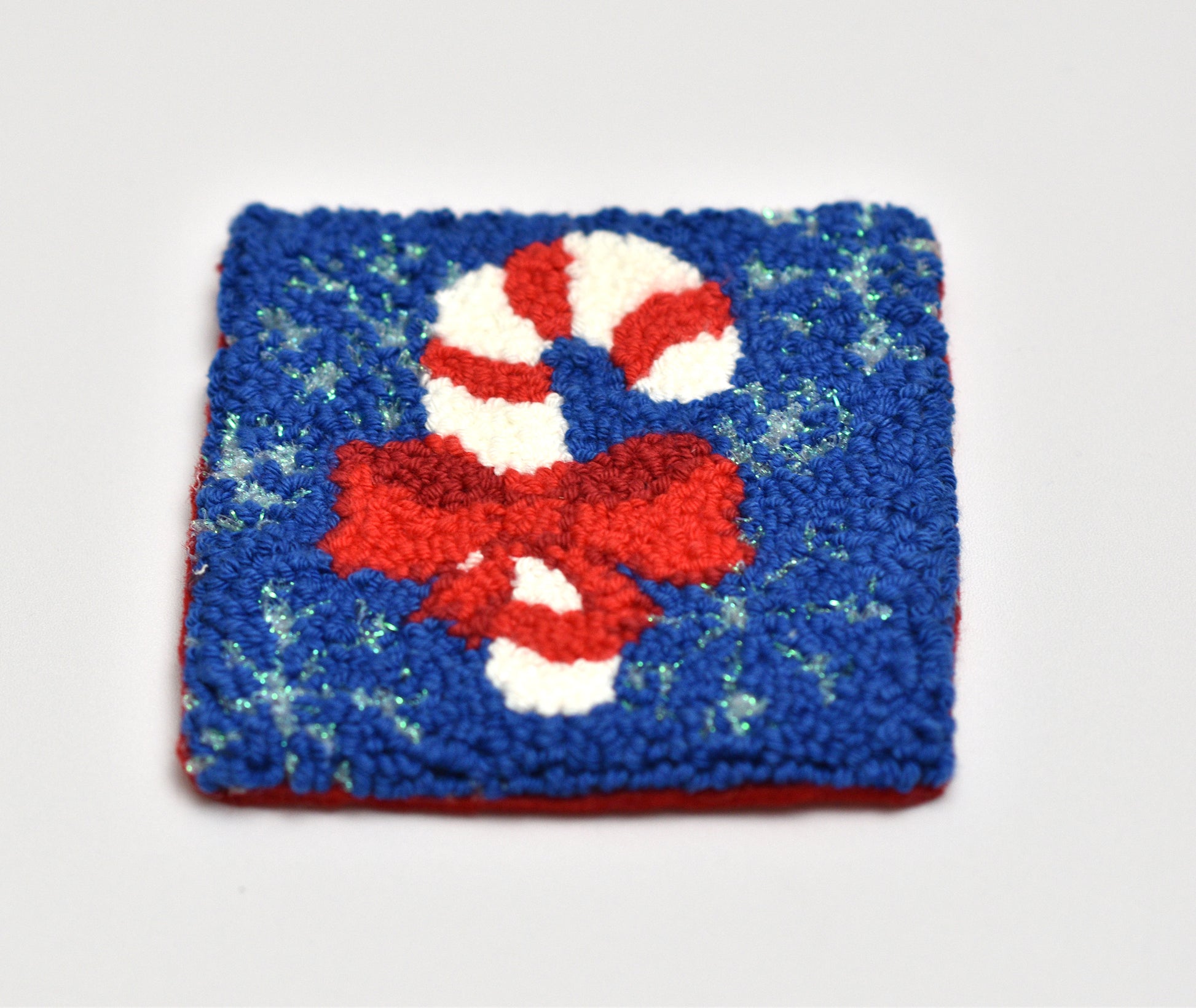 Punch needled coaster with candy cane design on a blue background