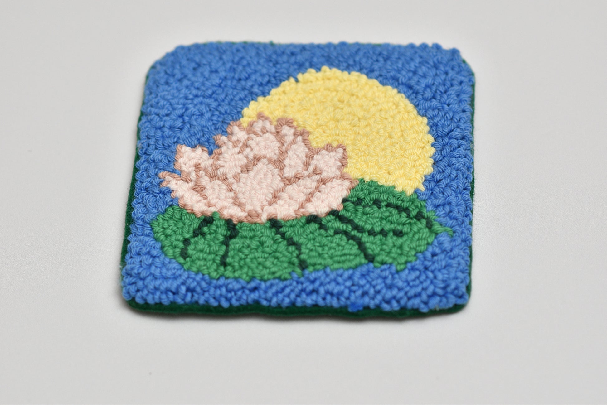 Square woven coaster with floral lily design on a plain background