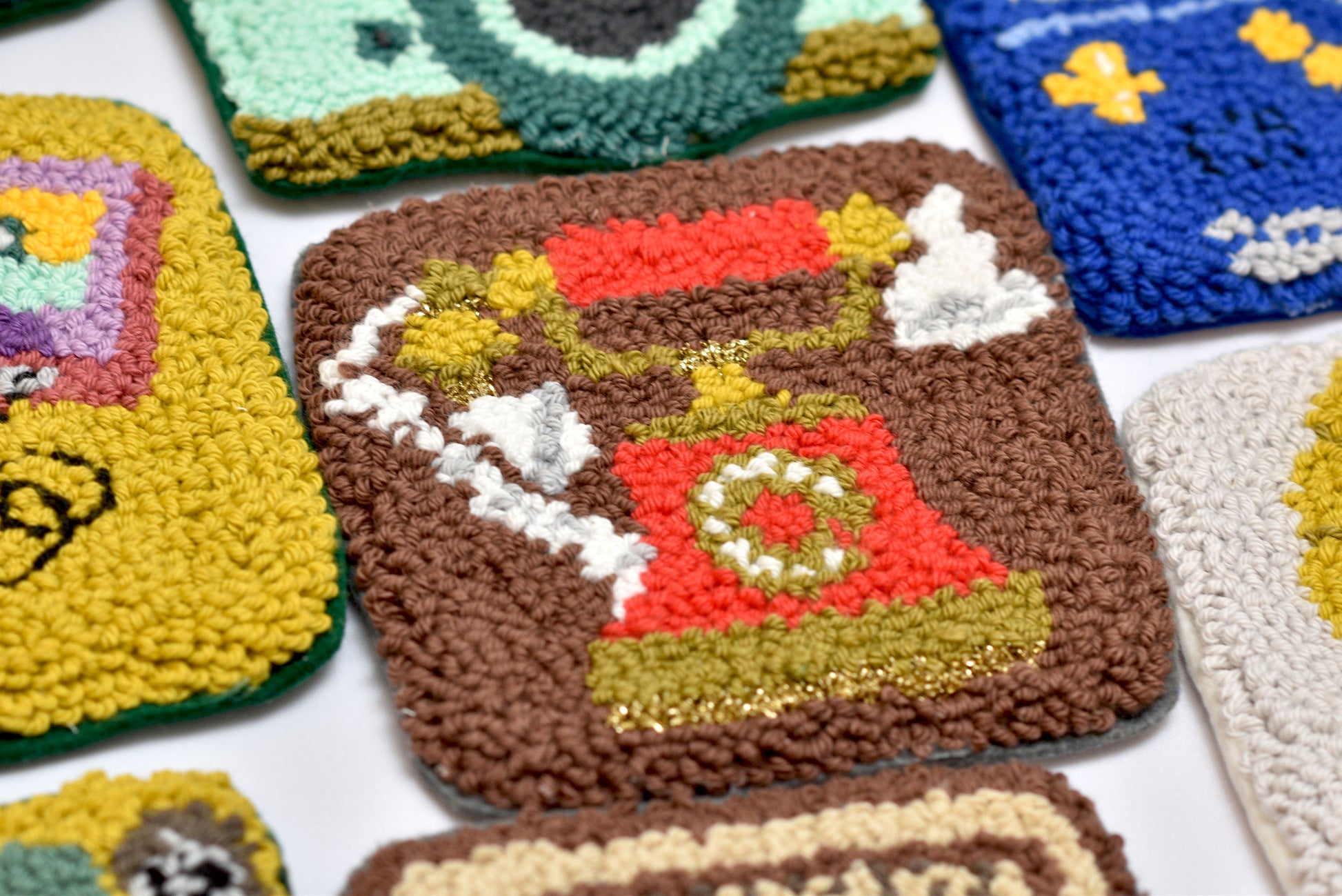 Colorful punch needle square coaster designs on a white background
