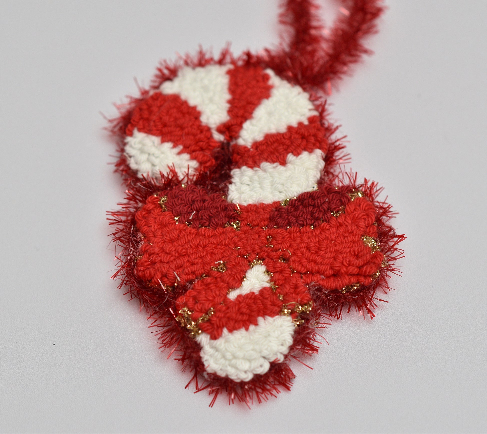 Punch needled candy cane ornament with red and white stripes on a light gray background
