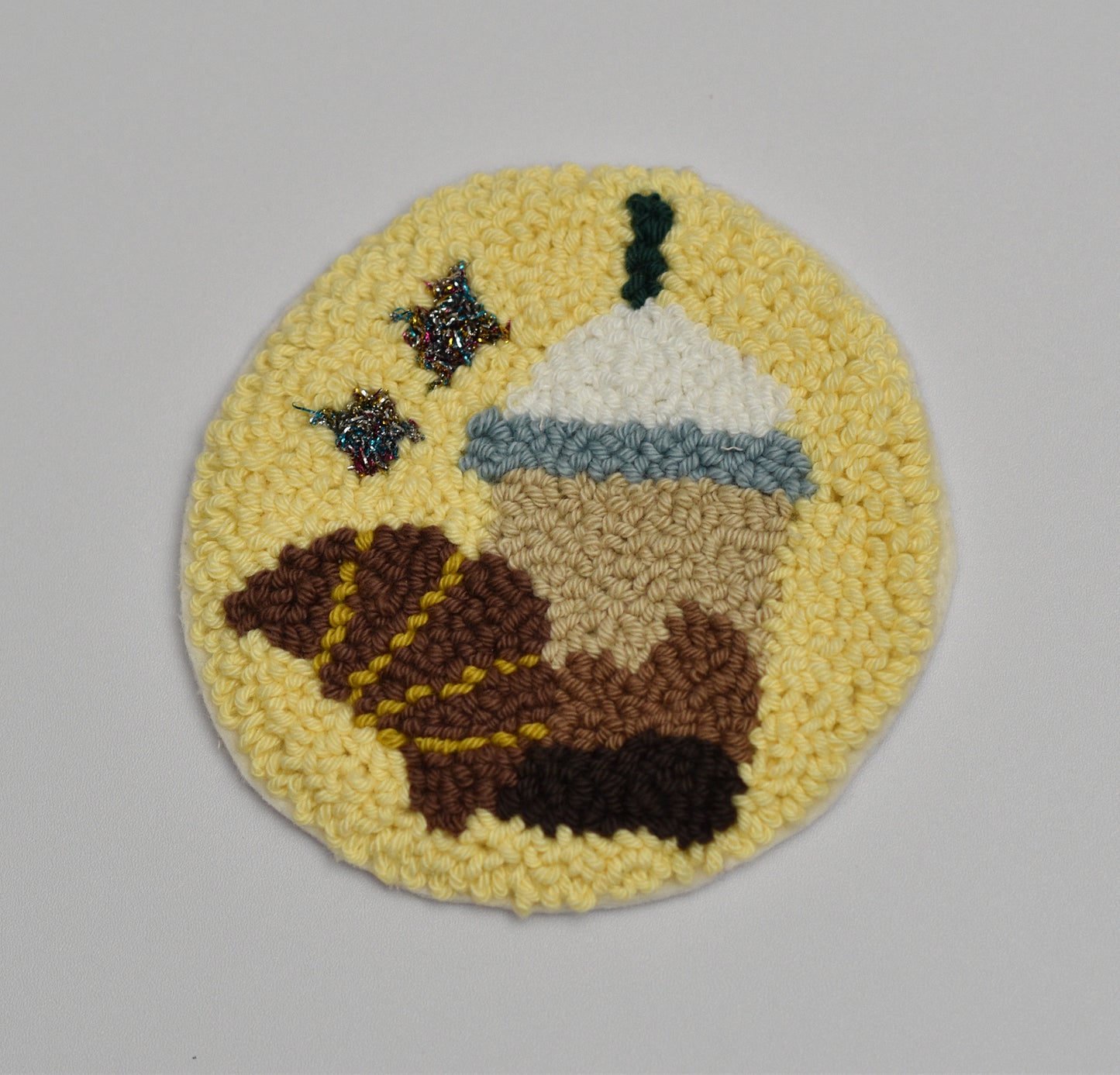 Circular embroidered coaster with a Coffee mug and croissant on a yellow background