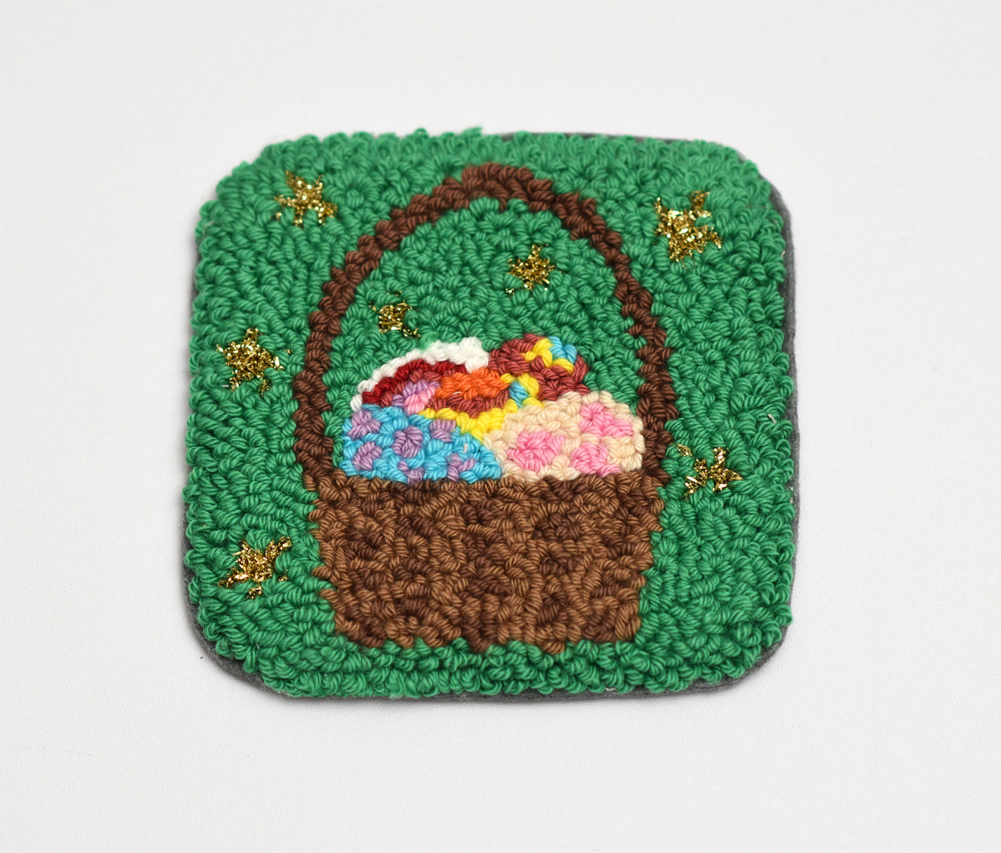 Embroidered coaster with a design of a brown basket with flowers on a green background
