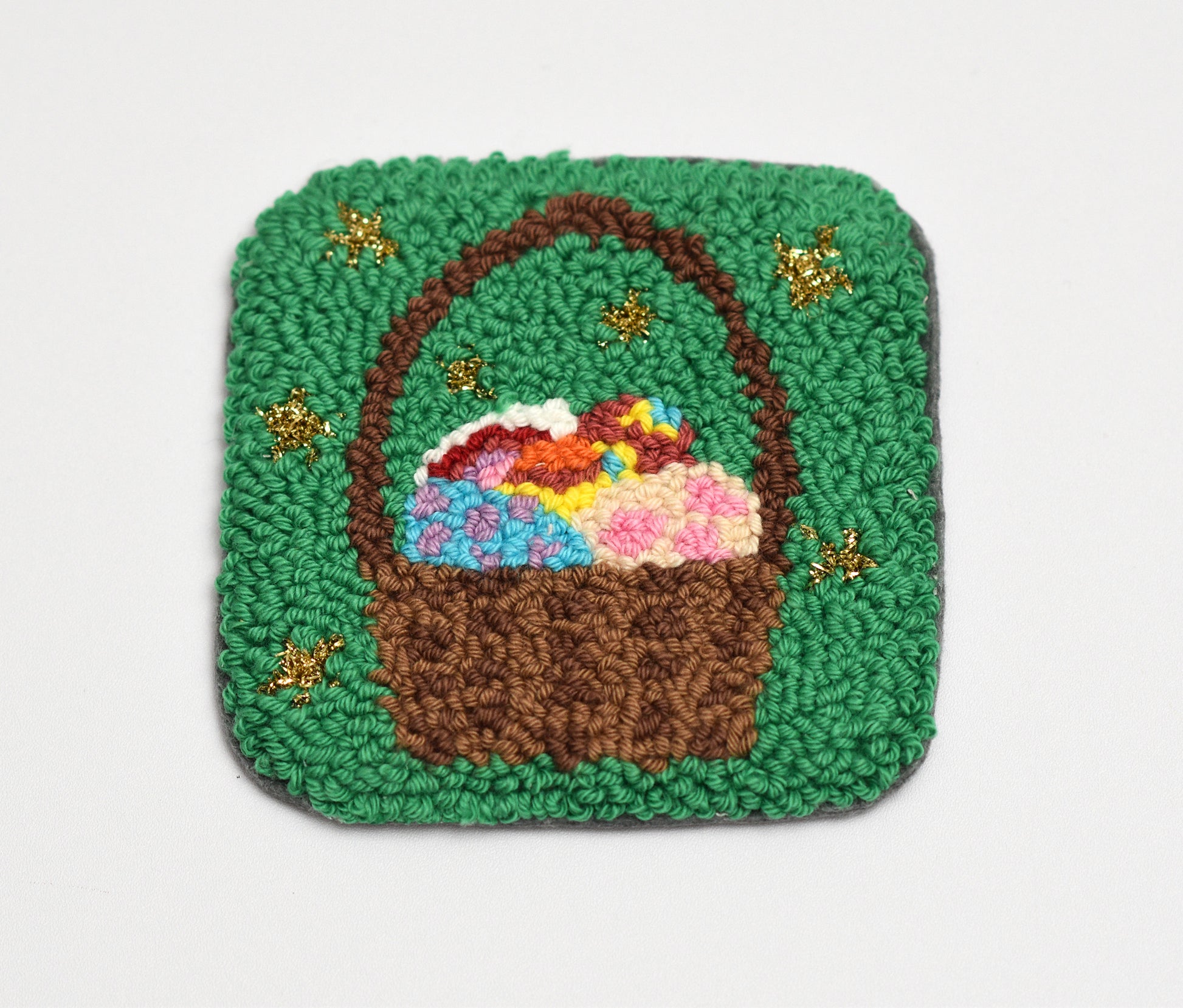 Embroidered coaster with a design of a brown basket with flowers on a green background