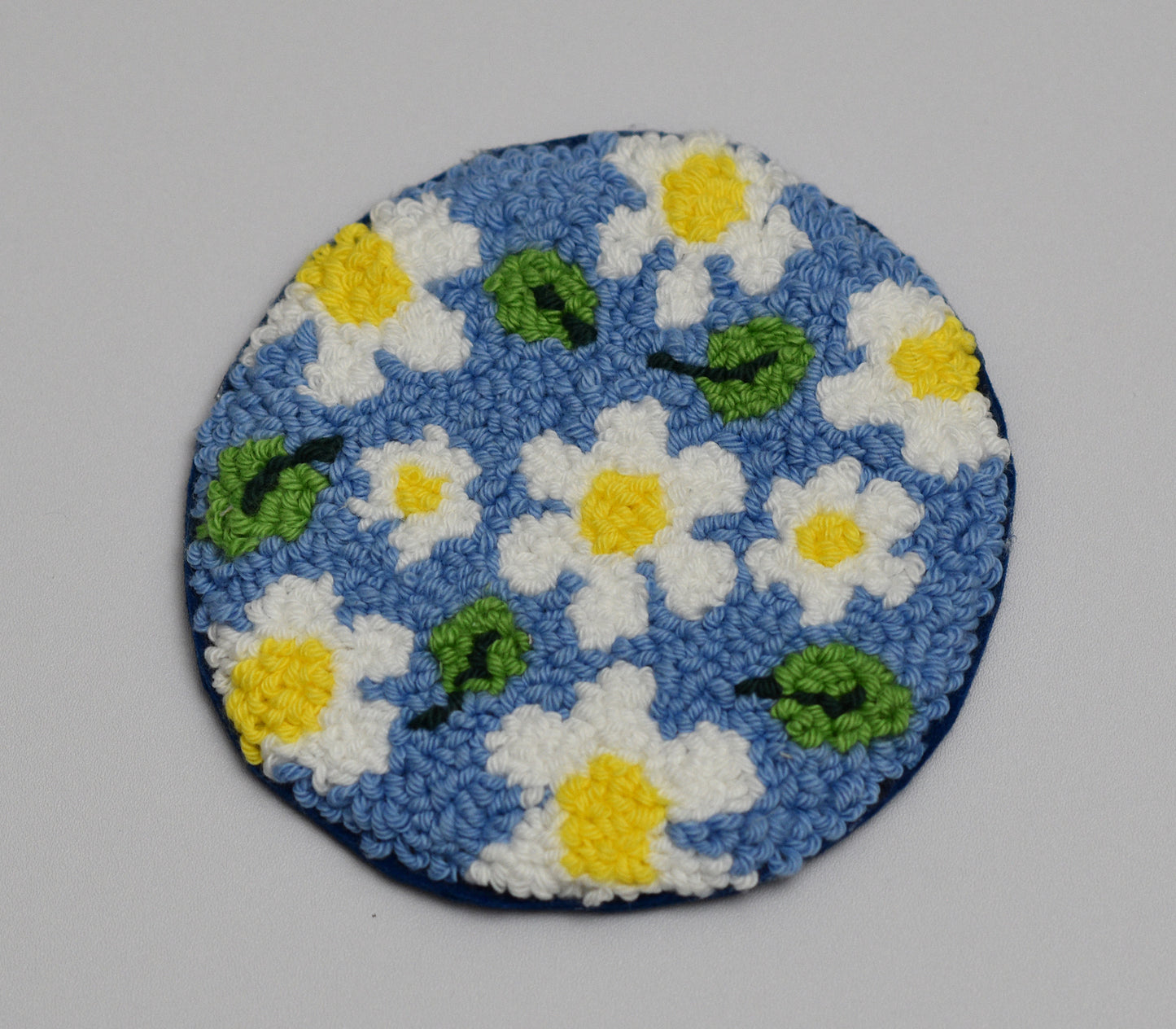 Circular embroidered coaster with daisy flowers on a blue background