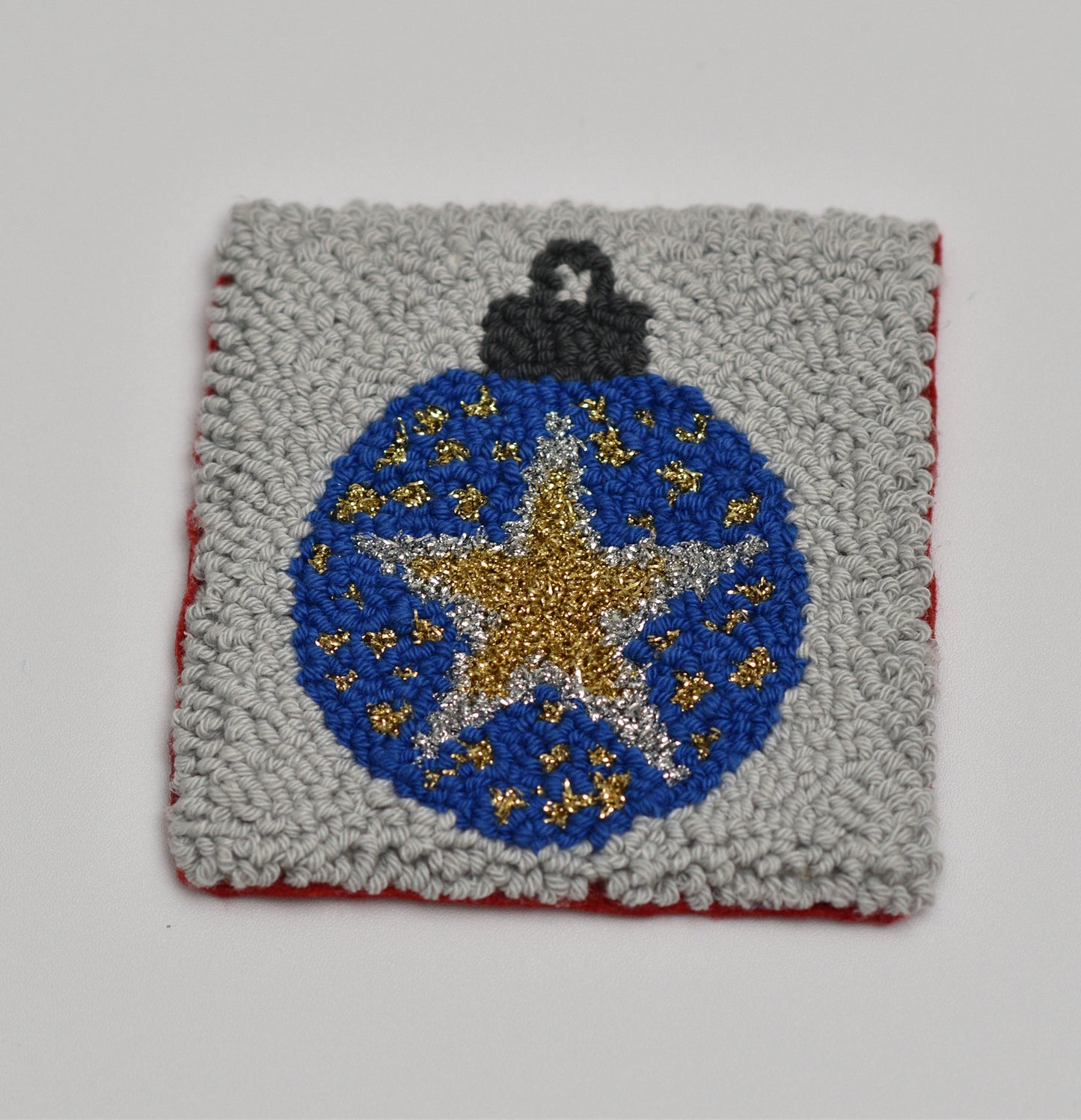 punch needled square coaster with a blue ornament featuring a star and gold accents on a gray background