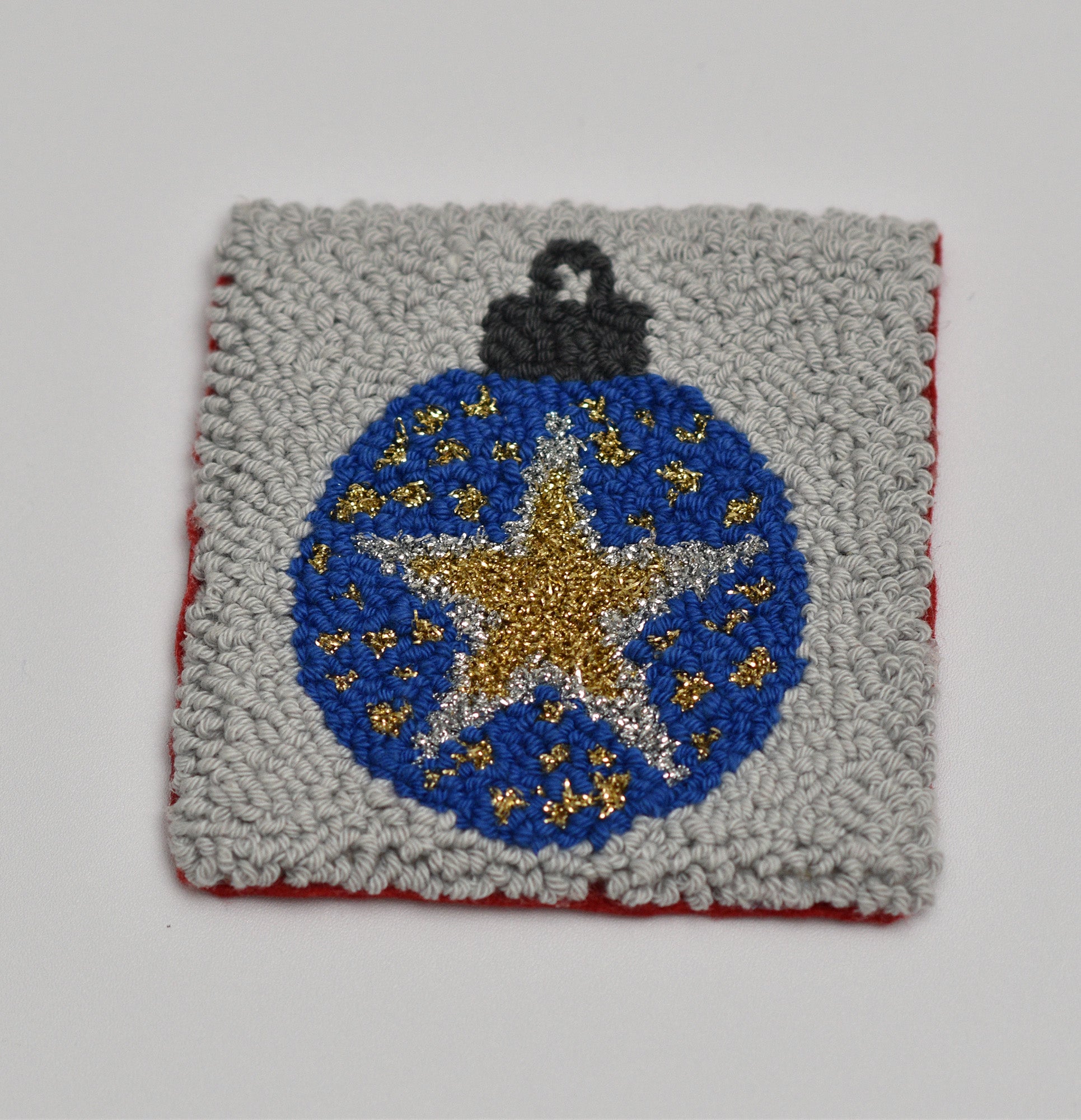 punch needled square coaster with a blue ornament featuring a star and gold accents on a gray background