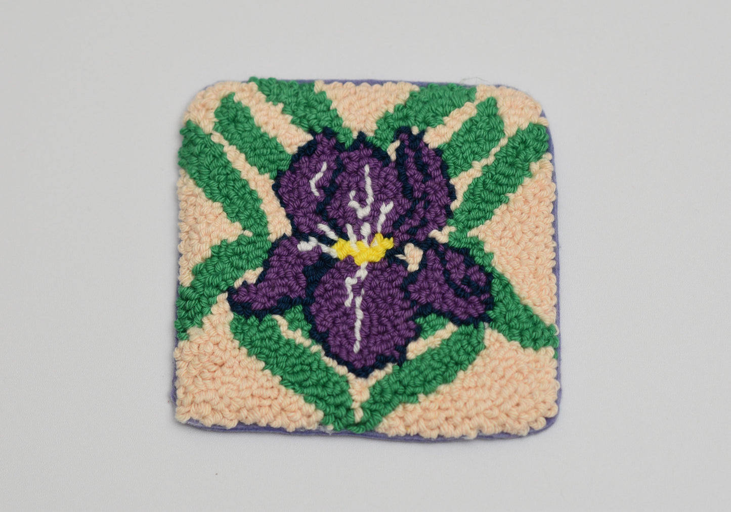 Decorative woven coaster with a purple iris flower design on a gray background