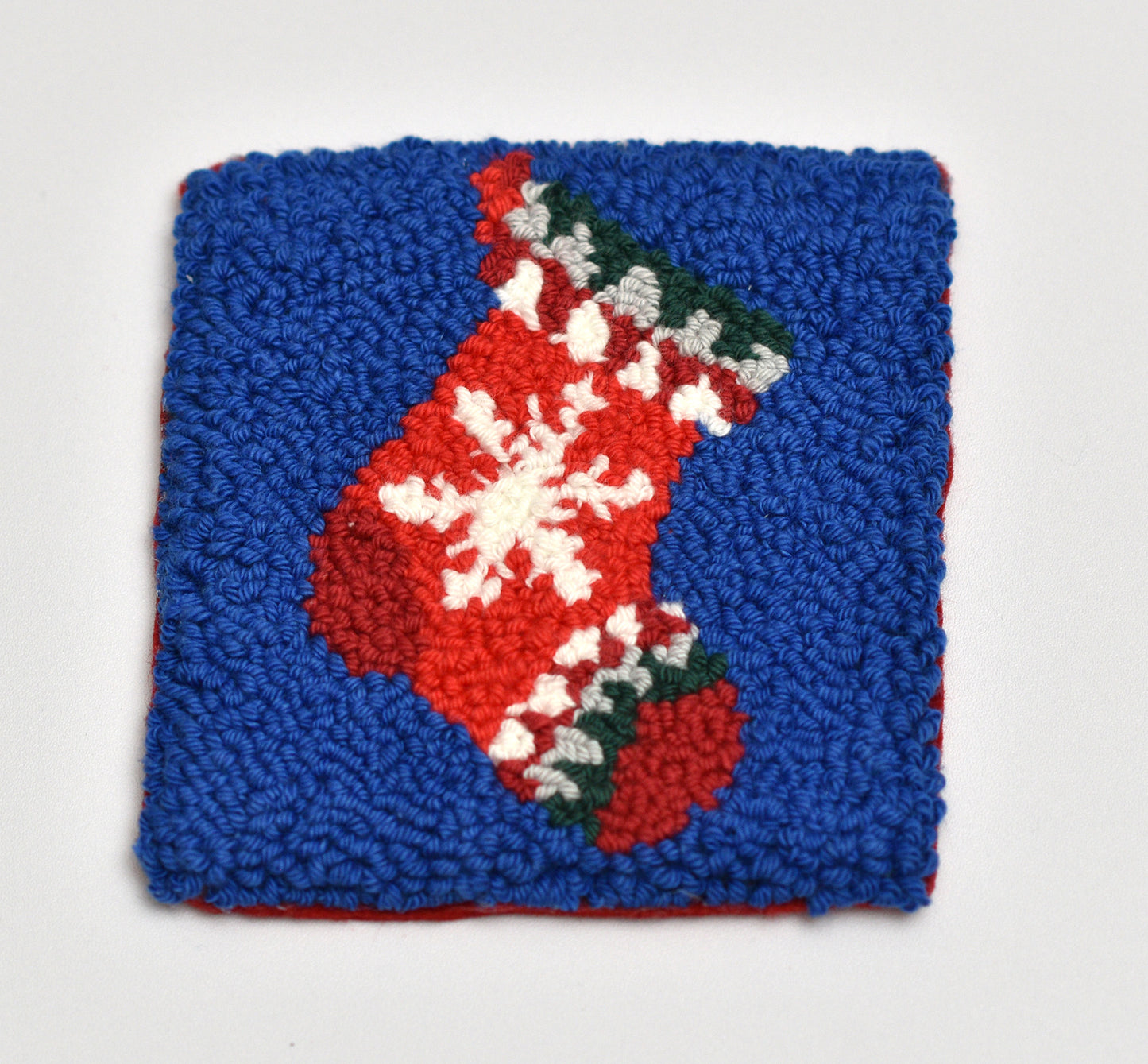 Punch needled square coasters with a red Christmas stocking design on a blue background
