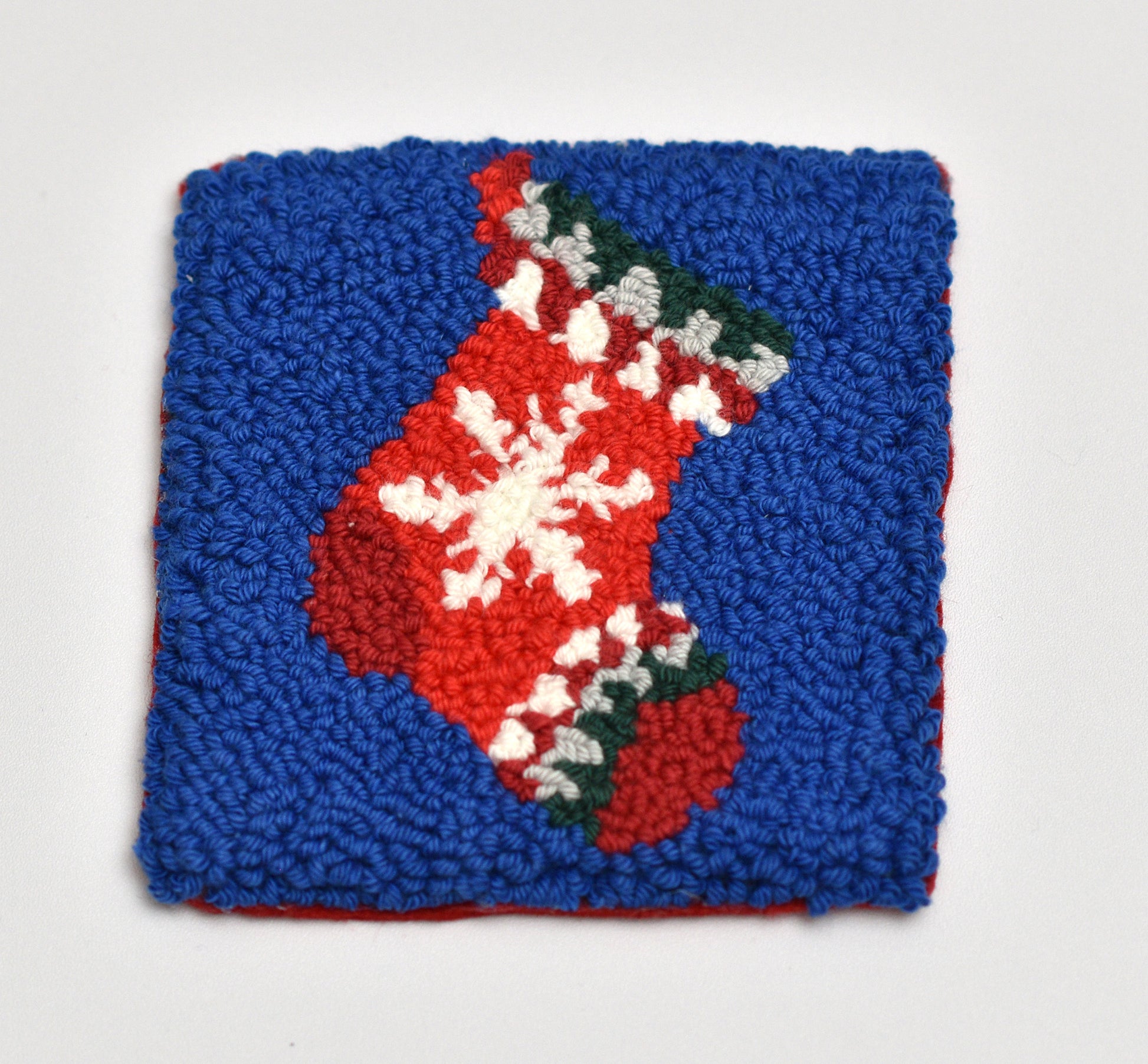 Punch needled square coasters with a red Christmas stocking design on a blue background