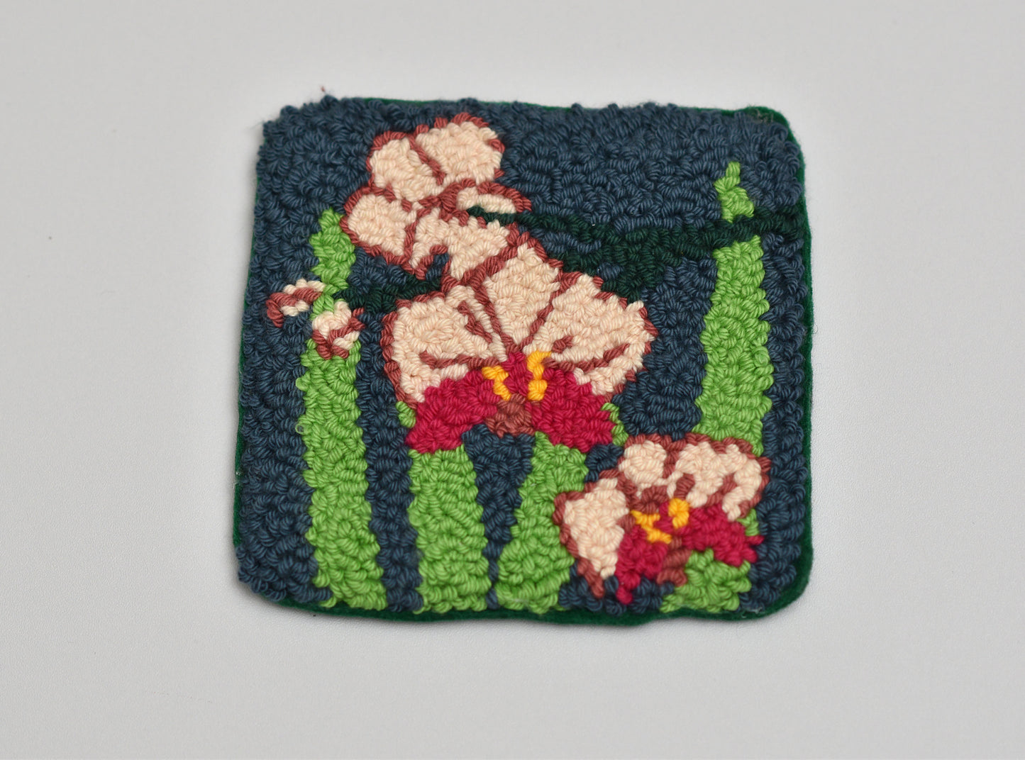 Punch needled square with floral orchid design on a gray background