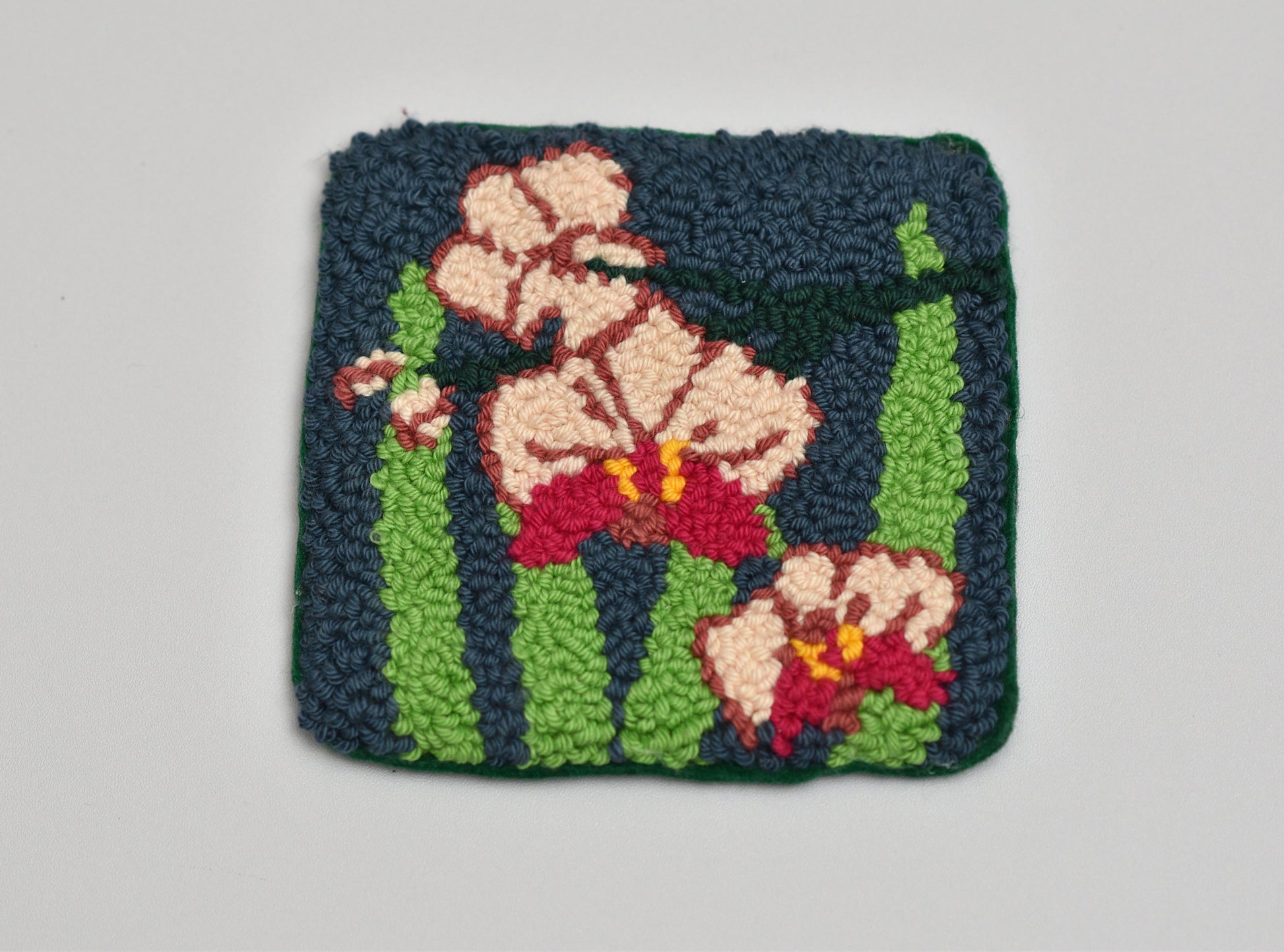 Punch needled square with floral orchid design on a gray background