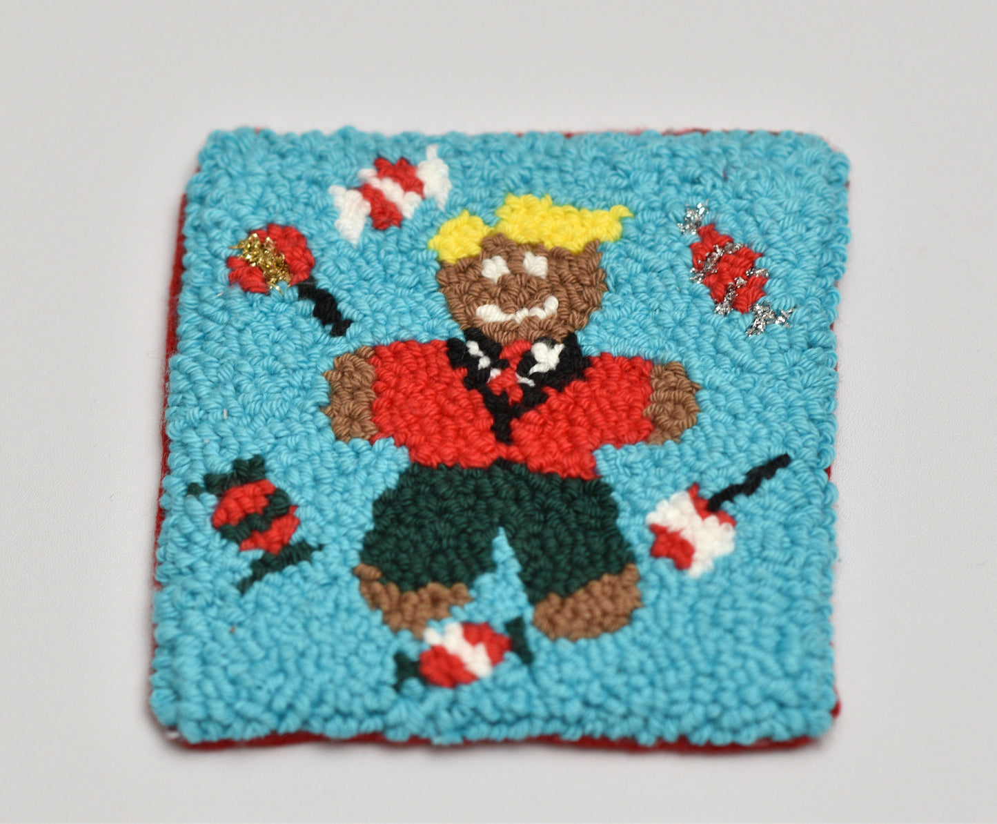 Punch needle coasters with a colorful design of a gingerbread man character holding lollipops on a light gray background