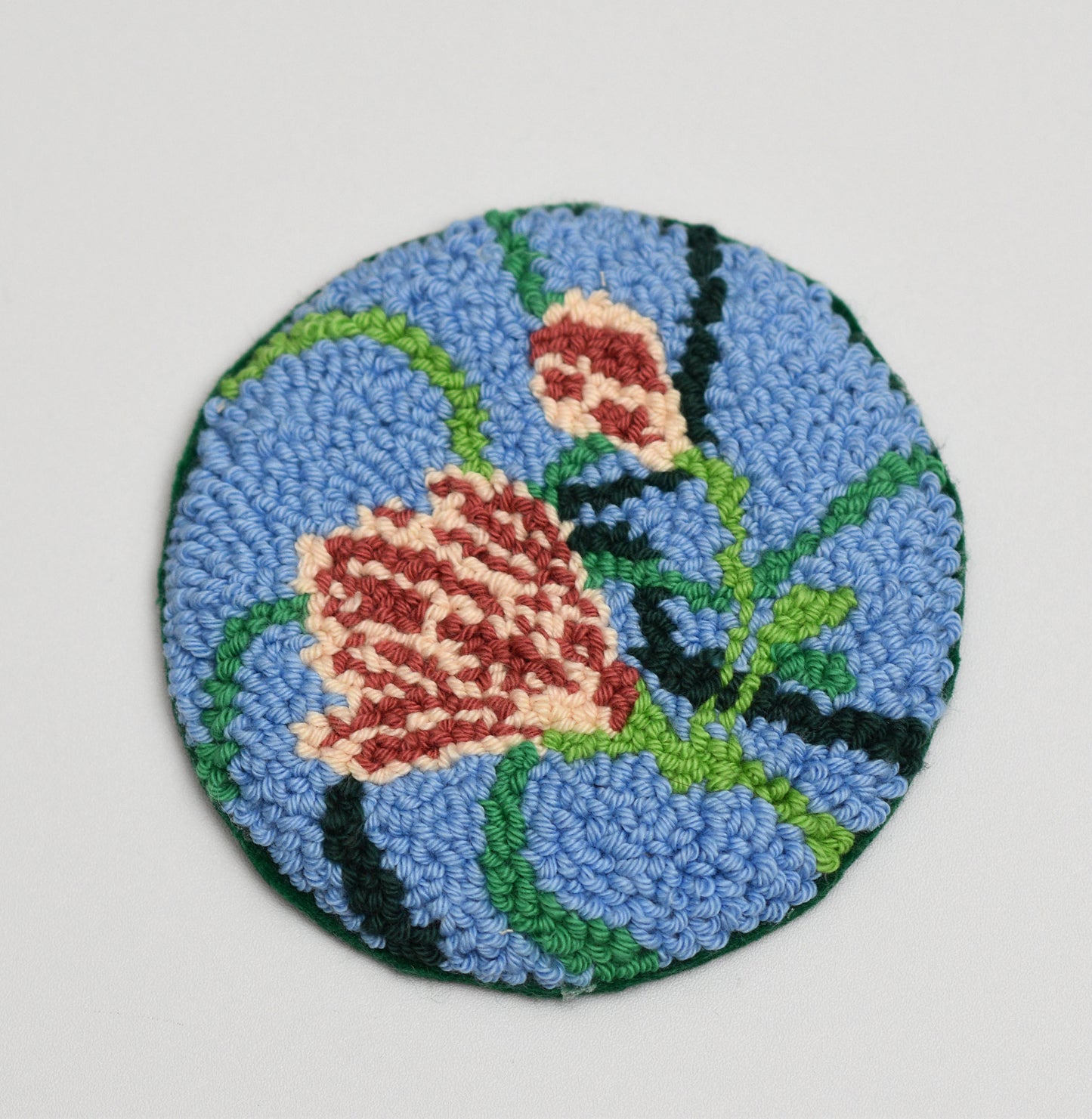 Round embroidered coaster with floral magnolia design on a blue background