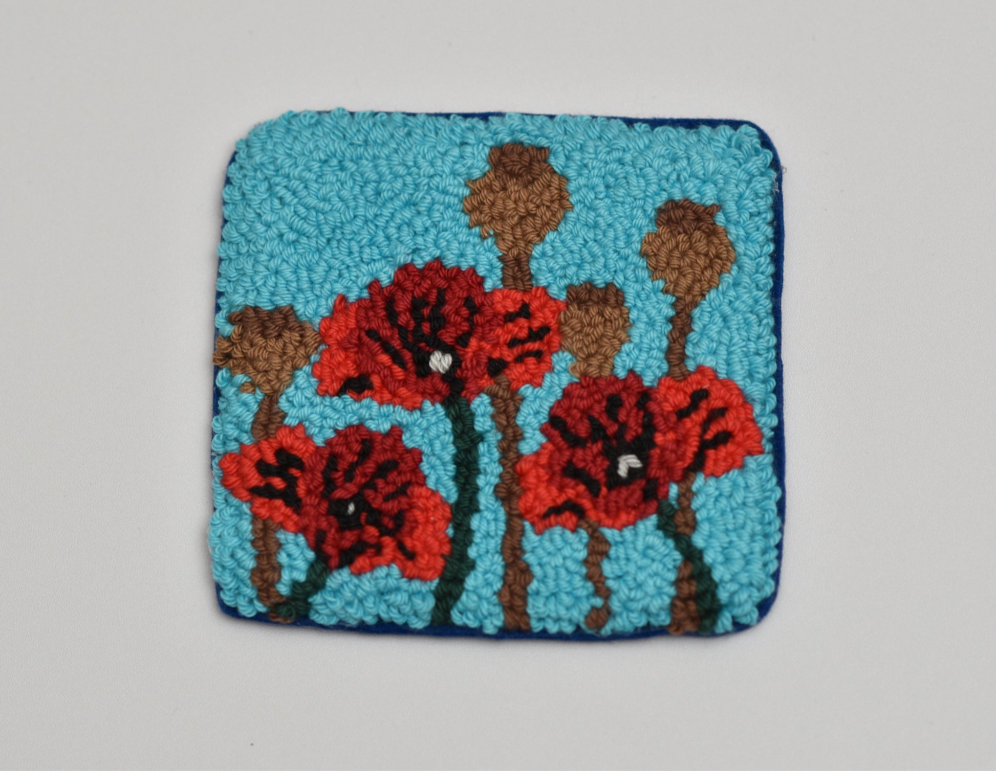 Embroidered coaster with red flowers and brown stems on a blue background