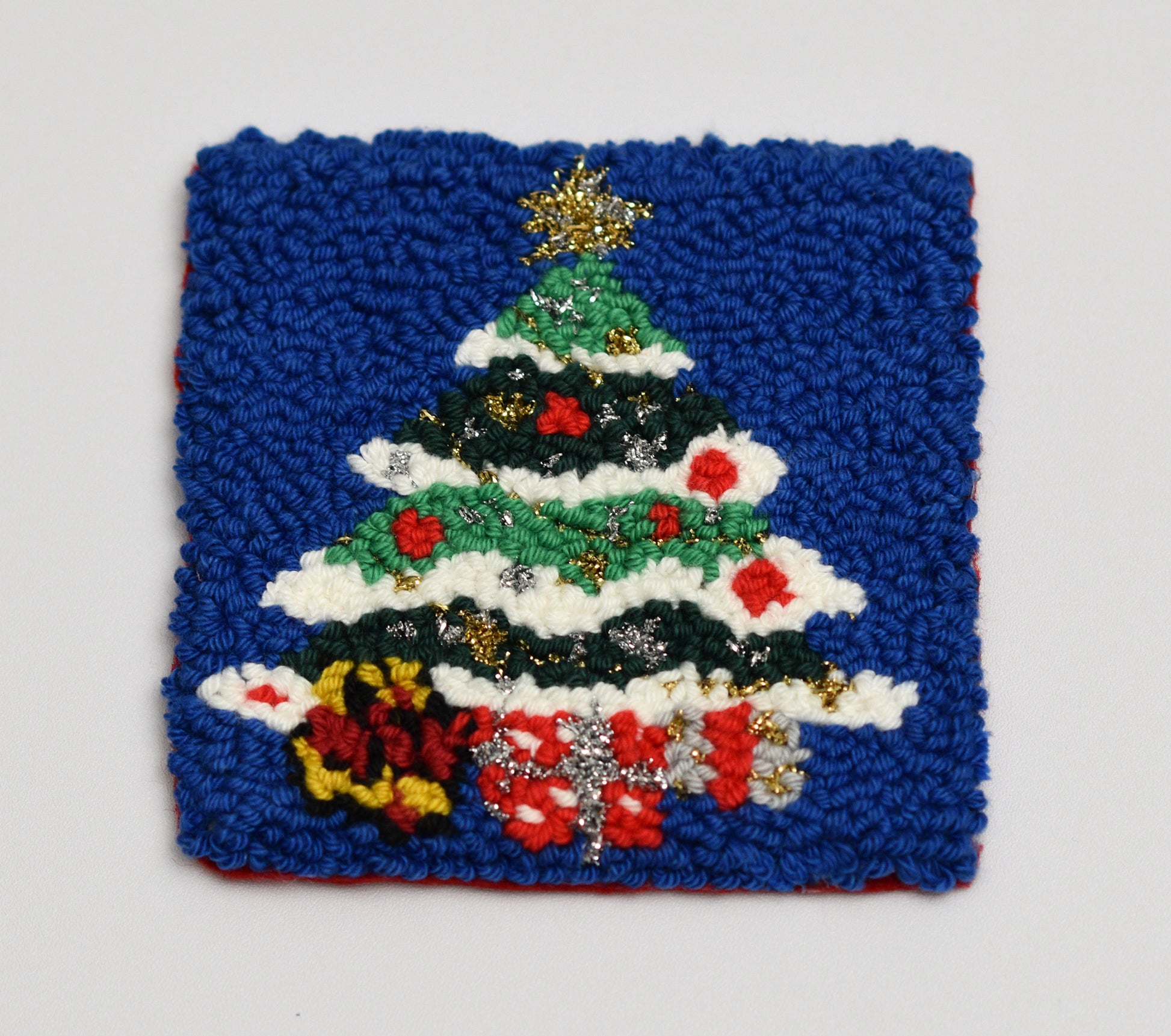 Embroidered coaster with Christmas tree design on a blue fabric background