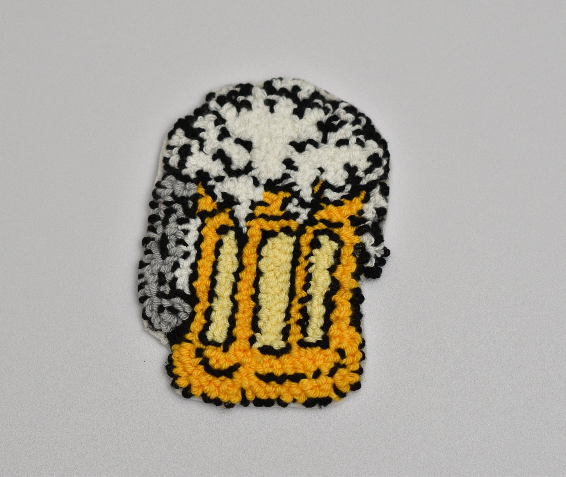 Embroidered coaster of a beer mug with foam on a gray background