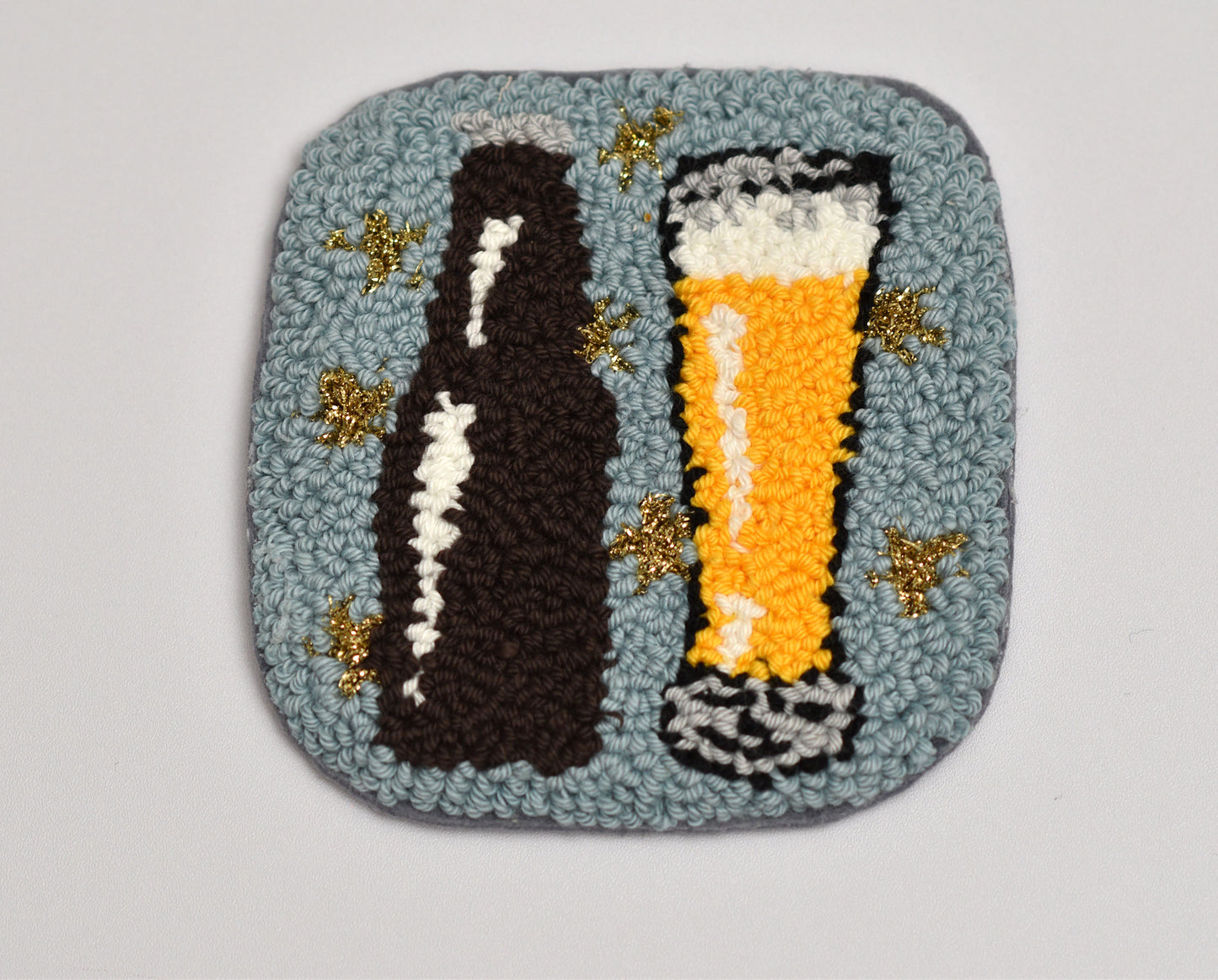 Embroidered coaster with a beer bottle and glass design on a light gray background
