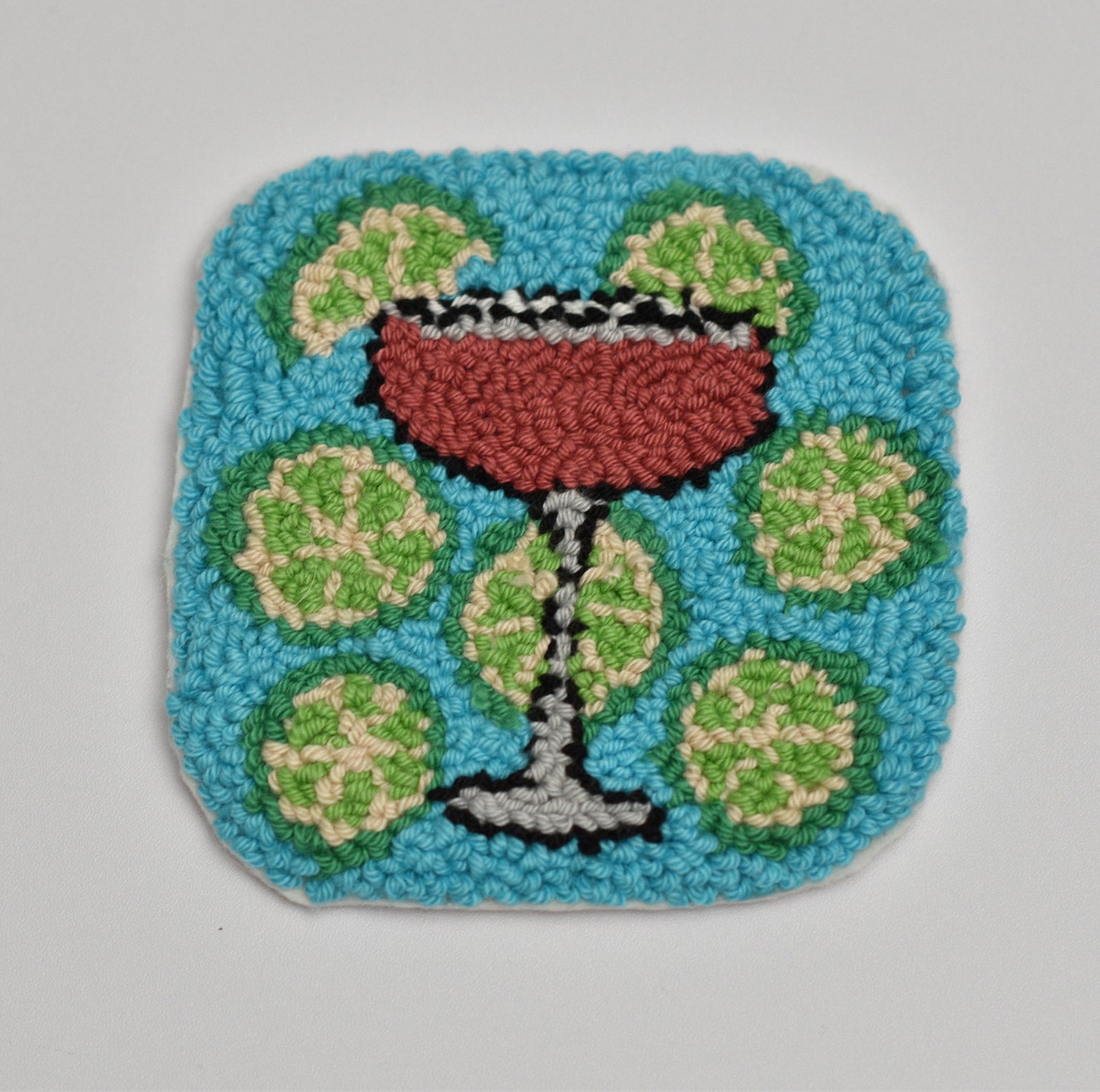Handmade mug rug coaster of a cocktail with limes on a blue background