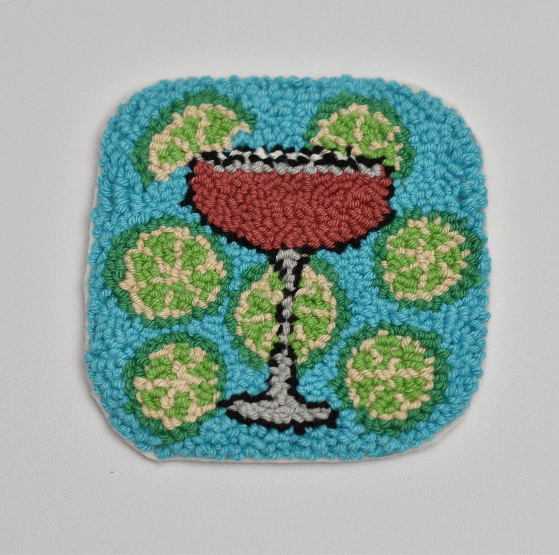 Handmade mug rug coaster of a cocktail with limes on a blue background