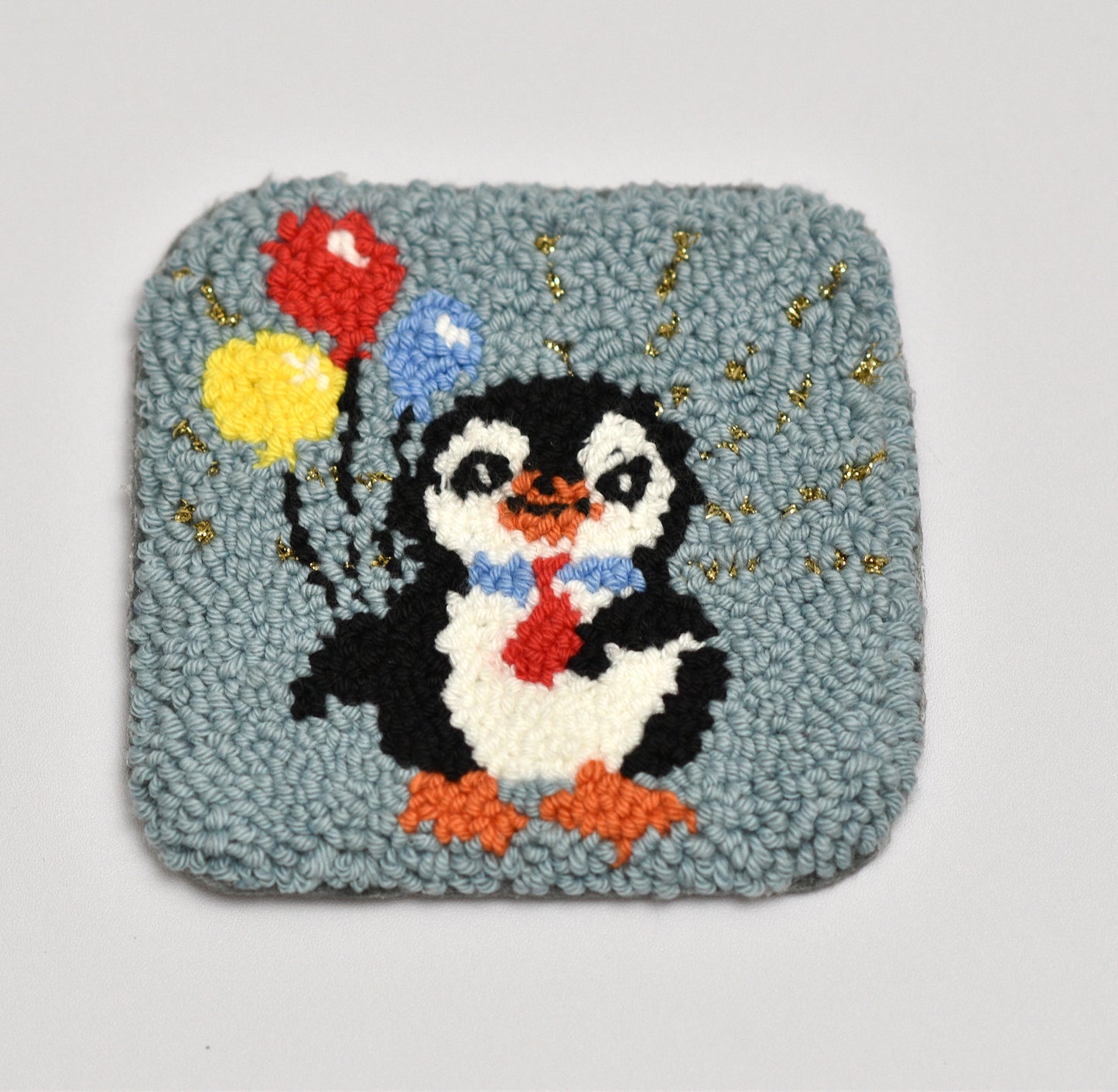 Penguin with balloons on a textured punch needled coaster