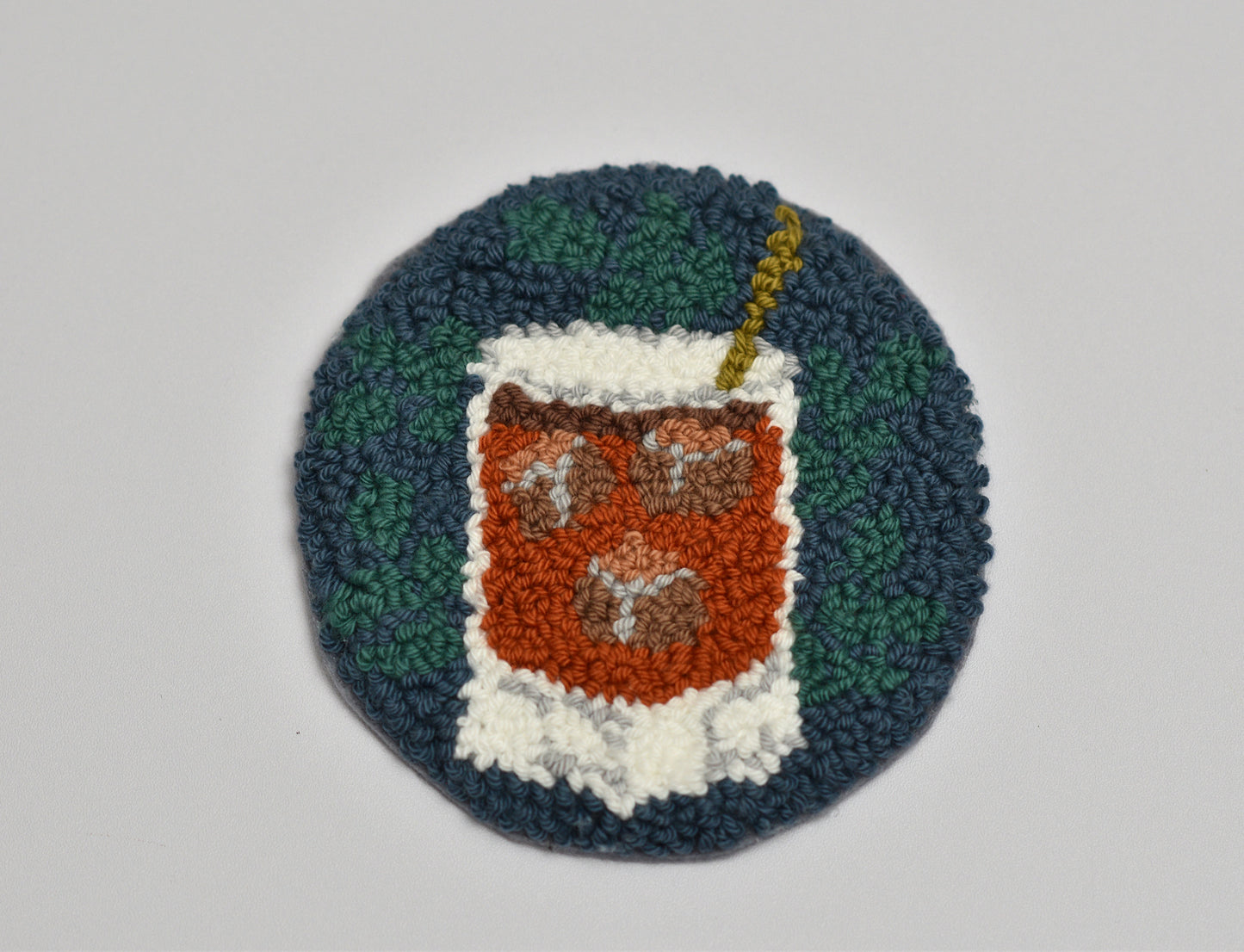 Circular woven coaster with a design of a Whiskey glass on a plain background