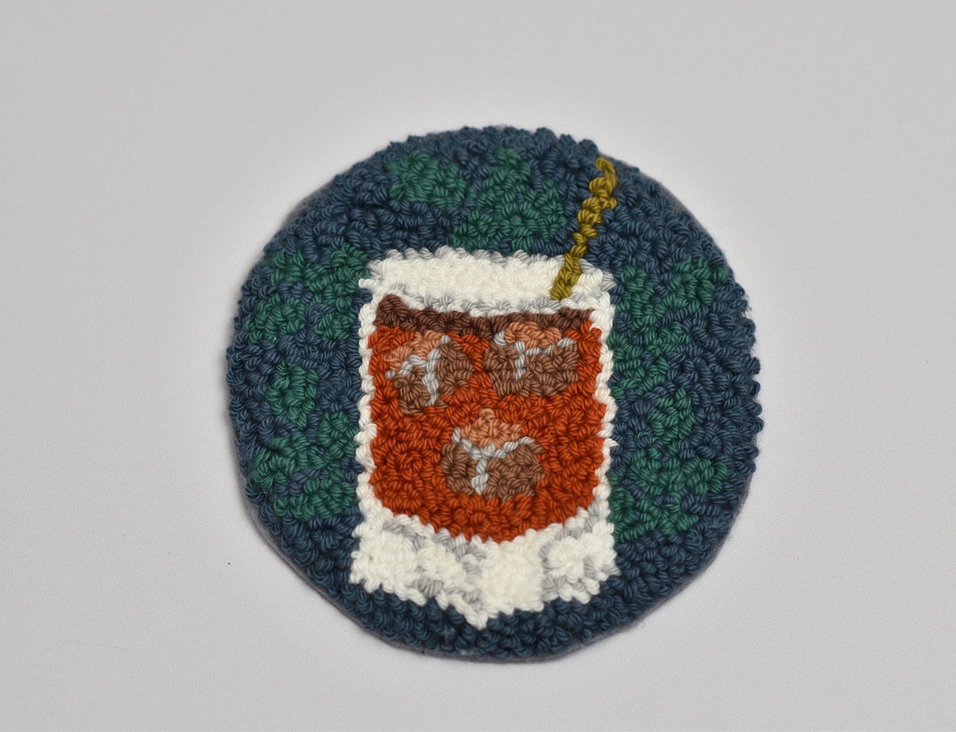 Circular woven coaster with a design of a Whiskey glass on a plain background