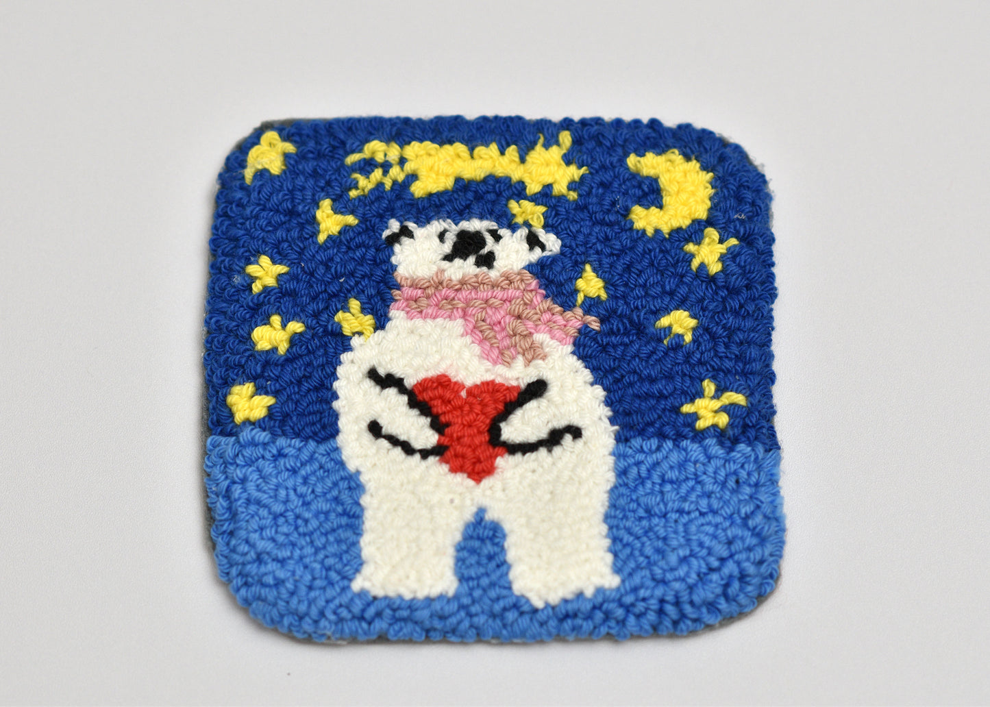 Square punch needled coaster with a cartoon character holding a heart, surrounded by yellow flowers on a blue background.