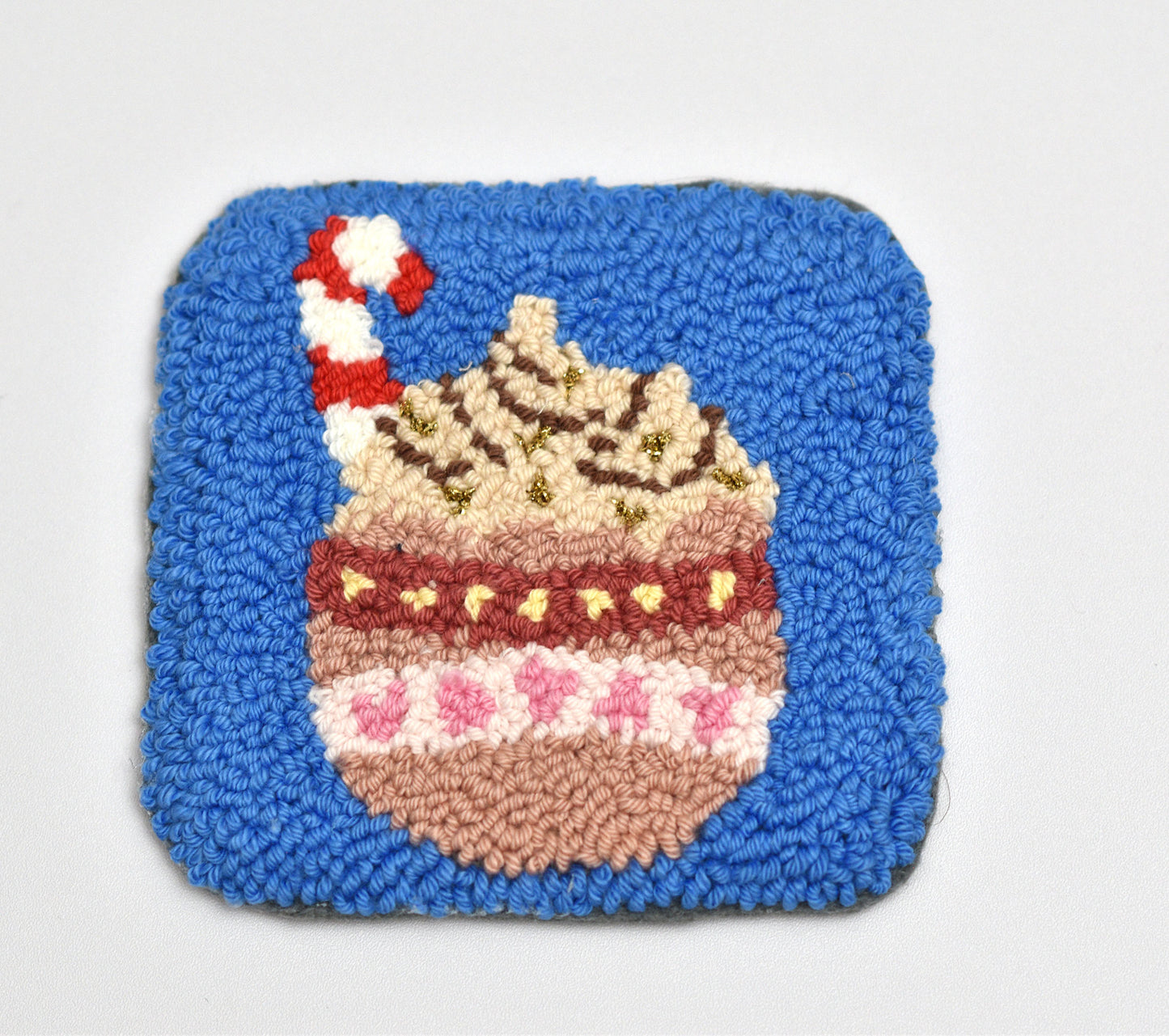Square woven coaster with a hot cocoa mug design on a blue background
