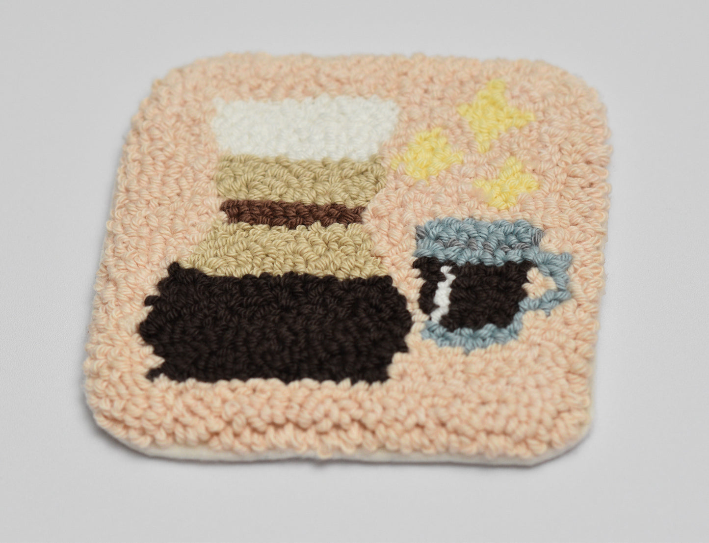 Punch needled square mug rug with coffee-themed design on a light gray background