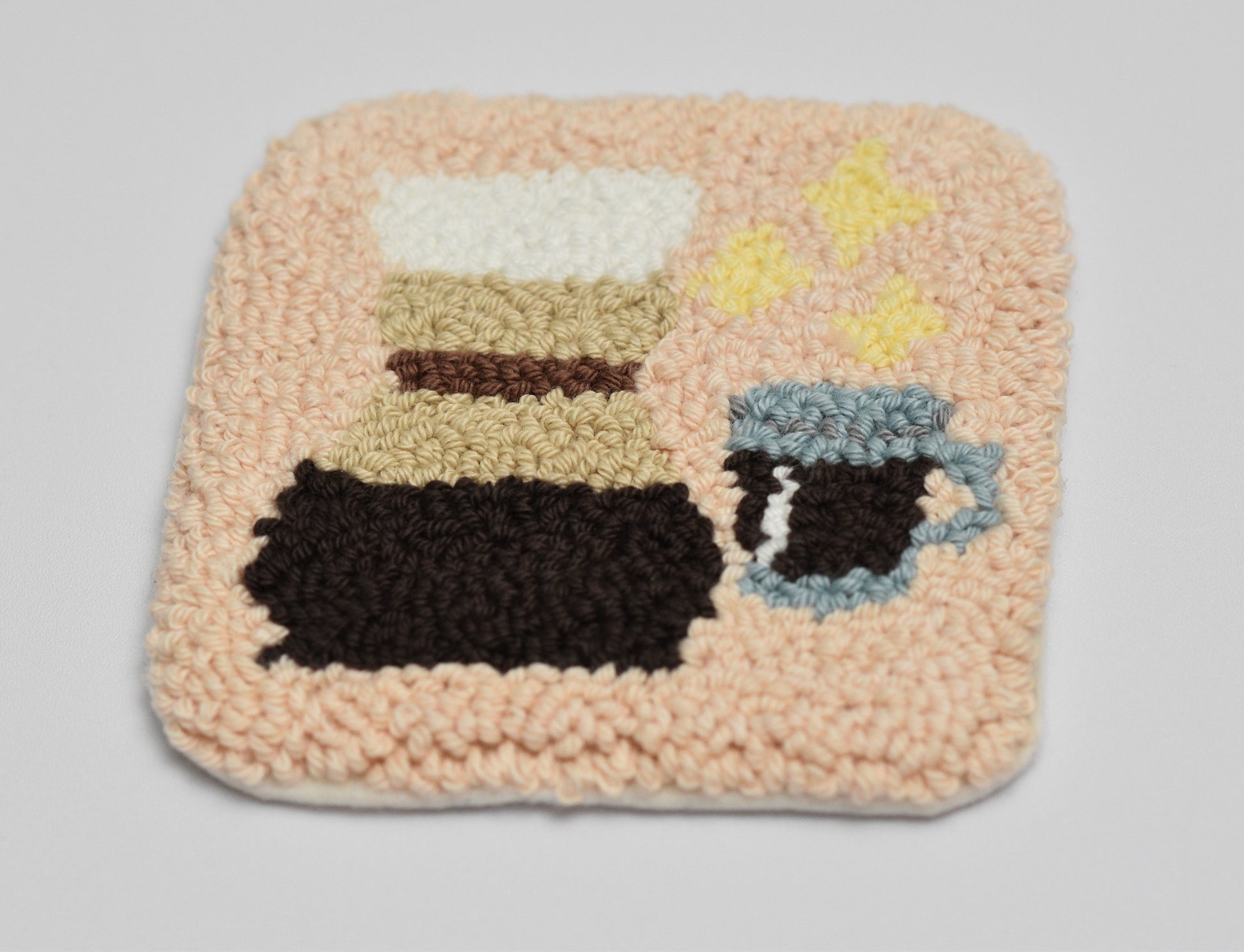 Punch needled square mug rug with coffee-themed design on a light gray background