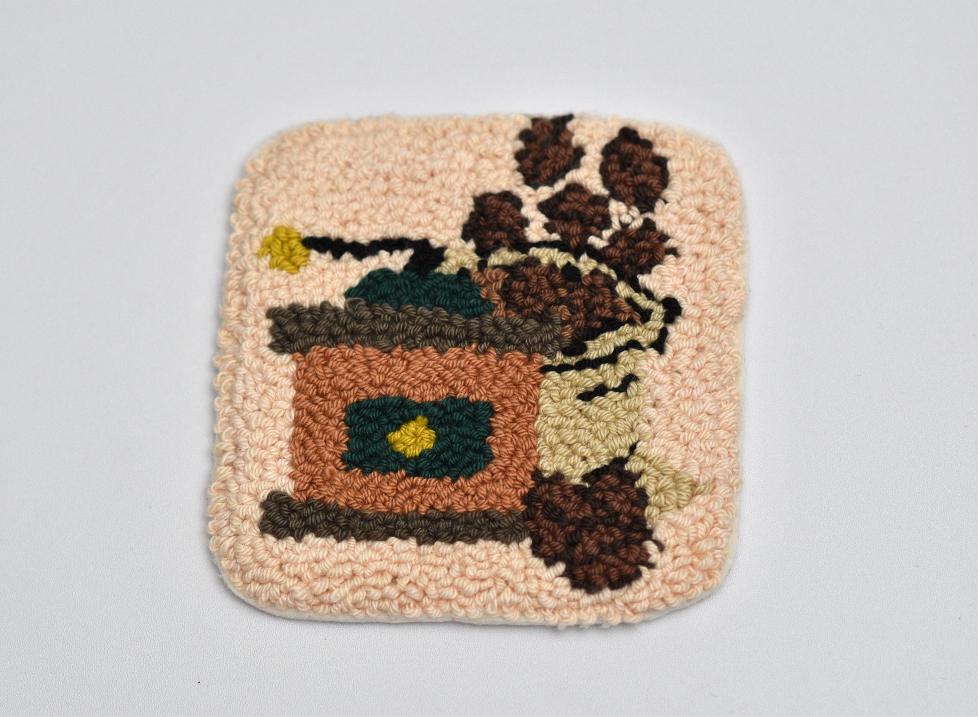 Punch needled square coaster with a coffee-themed design on a light gray background