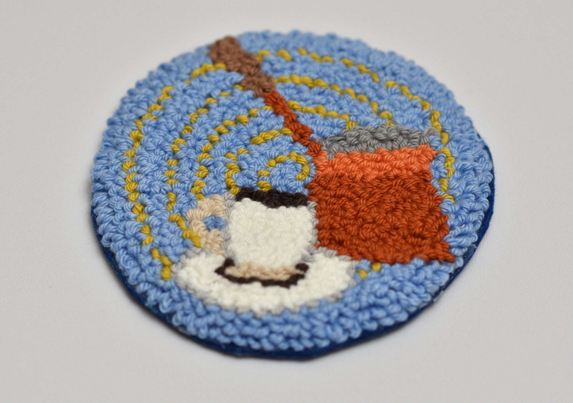 Round punch needle coaster with Turkish coffee-themed design on a light gray background