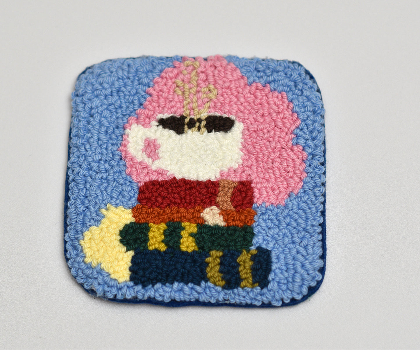 Colorful punch needled coaster with books and coffee cup design on a light gray background